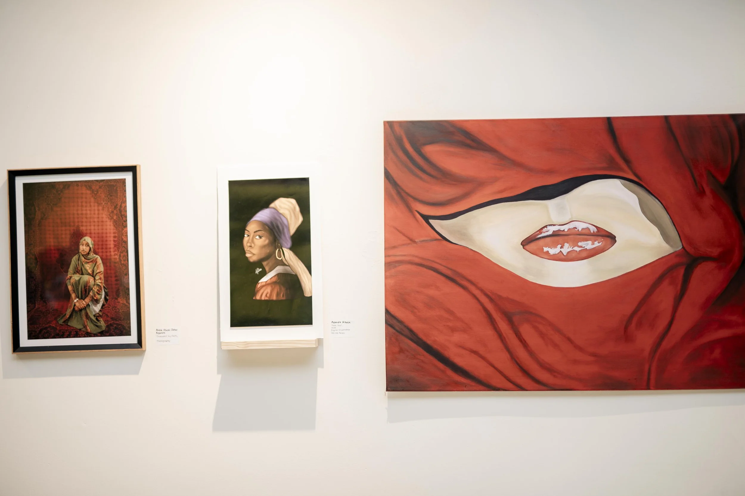 Art gallery display featuring multiple portraits, including a woman in traditional attire, a woman with head wrap, and an abstract piece with lips.