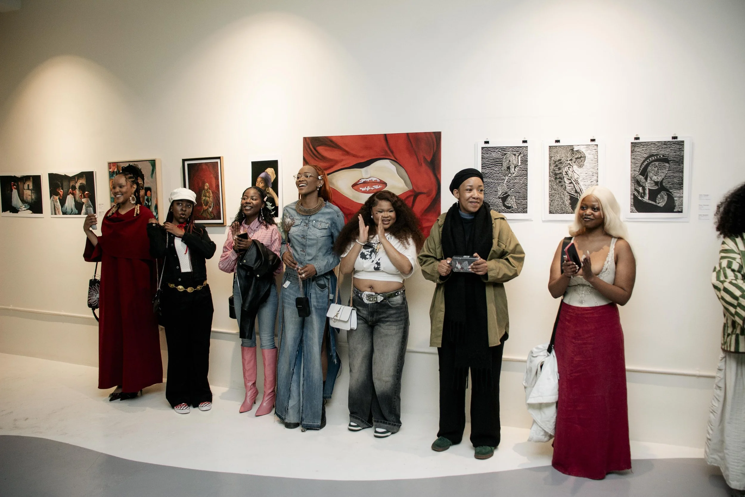 A group of diverse people standing in an art gallery, smiling and looking at artwork on the wall behind them.