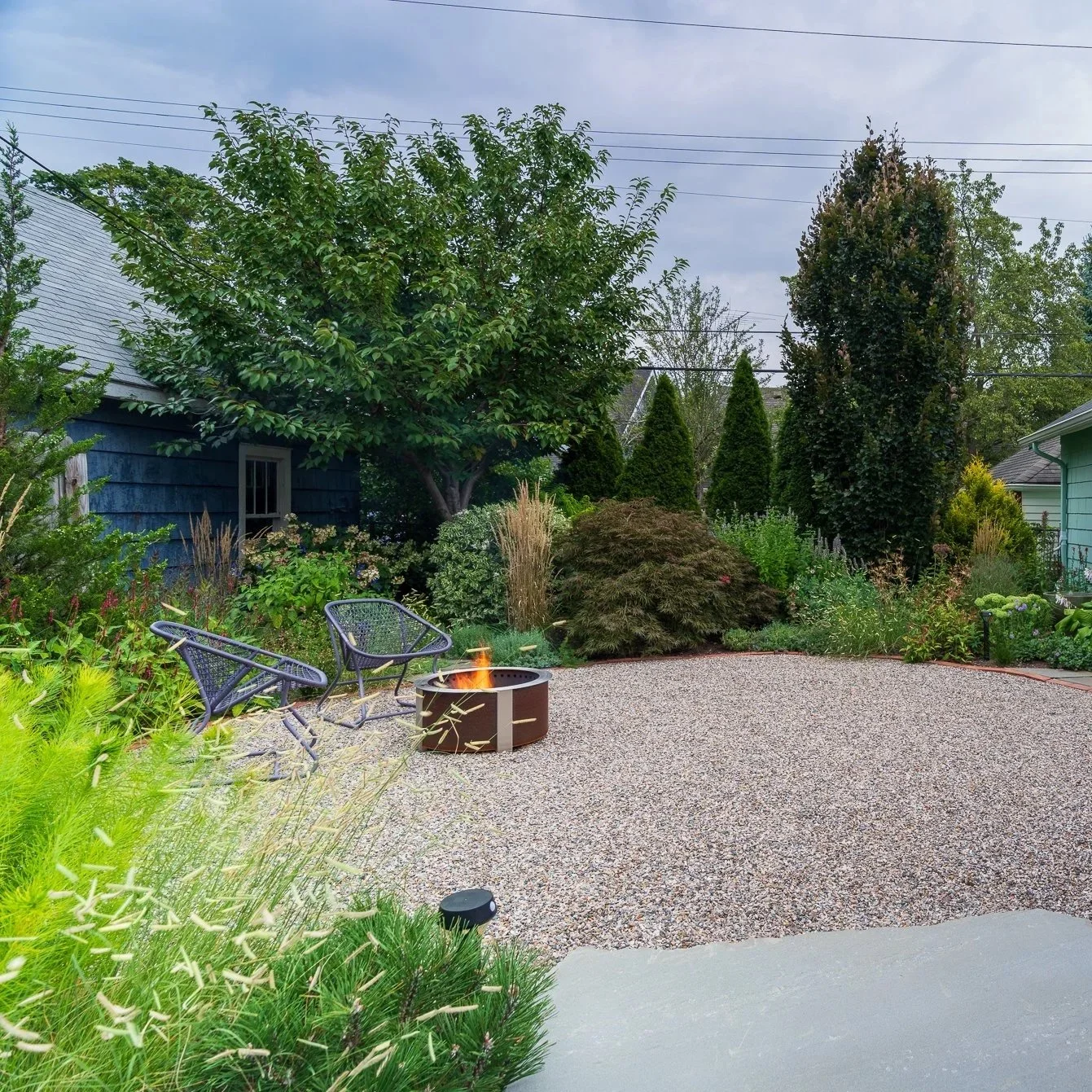 Award-winning naturalistic backyard landscape with gravel patio, fire pit, ornamental grasses, and layered native-inspired planting design in Ann Arbor, Michigan.