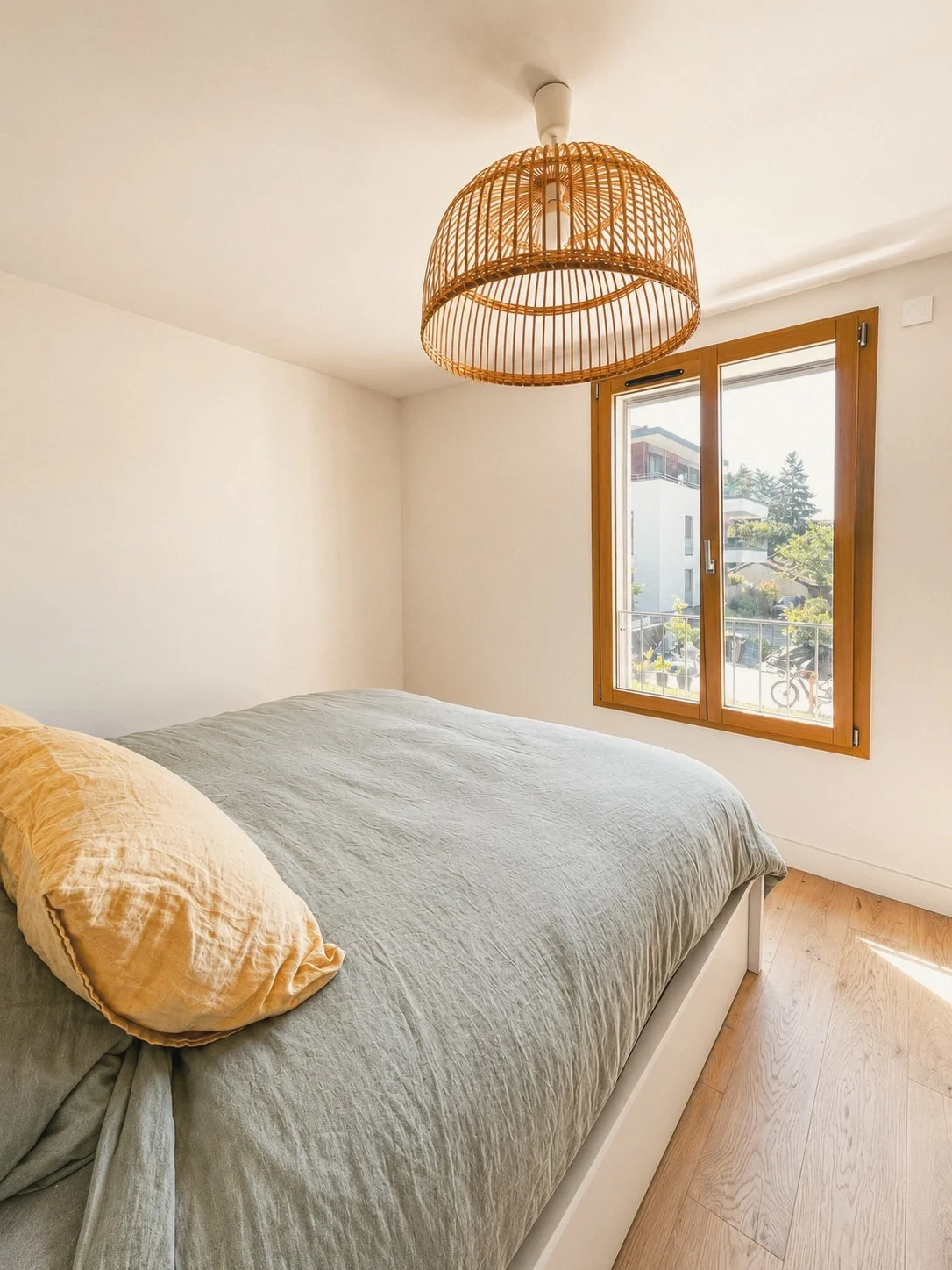 Chambre avec un lit à coucher, unique fenêtre en bois, luminaire en rotin au plafond, sol en bois clair.
