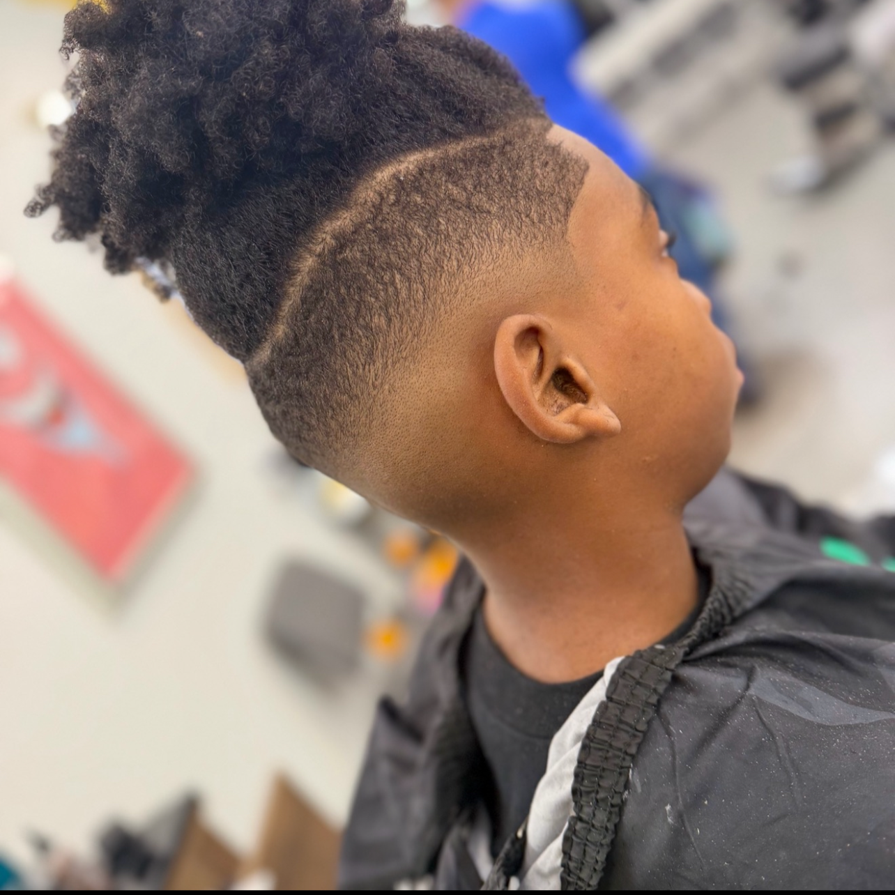 A young person with a high fade haircut and a curly top hairstyle in a barbershop.