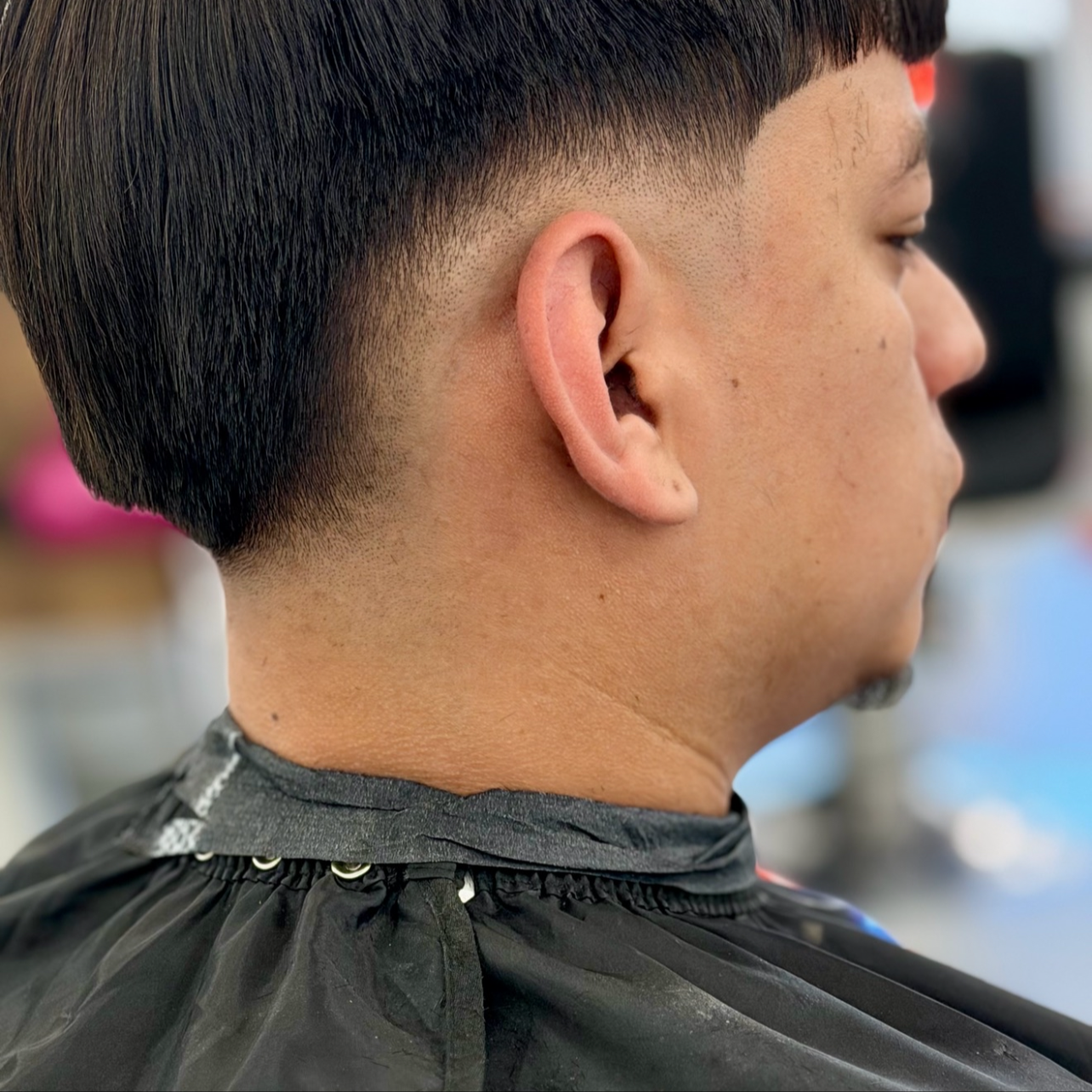 Side profile of a man with a modern, short haircut in a barbershop.