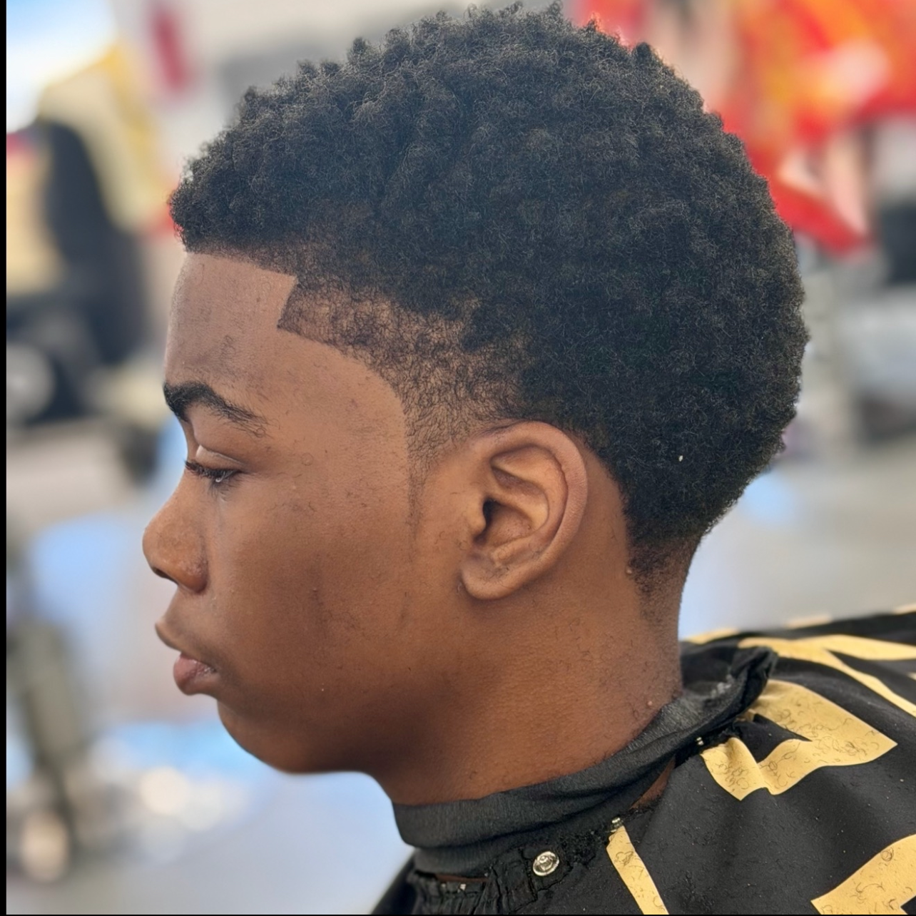 Side view of a young man with a fade haircut and curly natural hair on top, sitting in a barbershop.