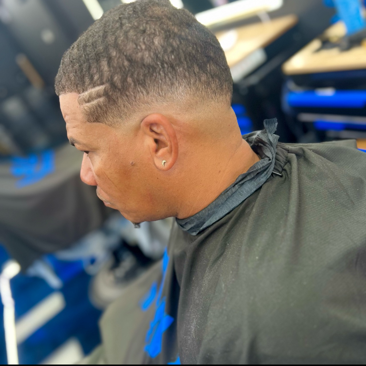 A man with a fresh fade haircut, wearing an earring, sitting in a barbershop.