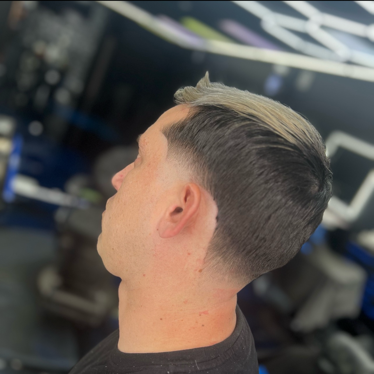 Side view of a man with a fresh undercut hairstyle, with dark hair on the sides and back, and longer, blonde hair on top.