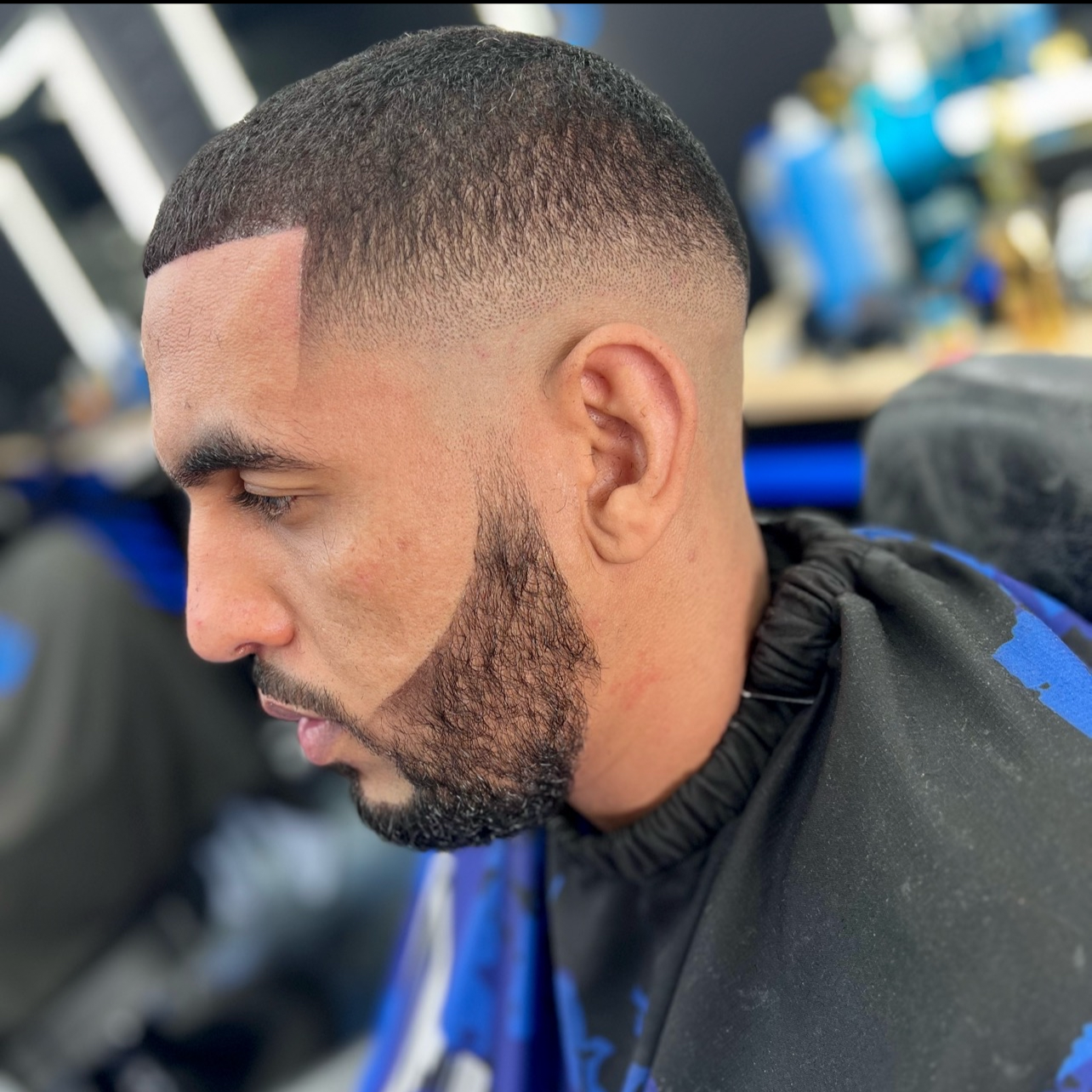 Close-up of a man with a fresh haircut, including a fade and a beard, sitting in a barbershop.