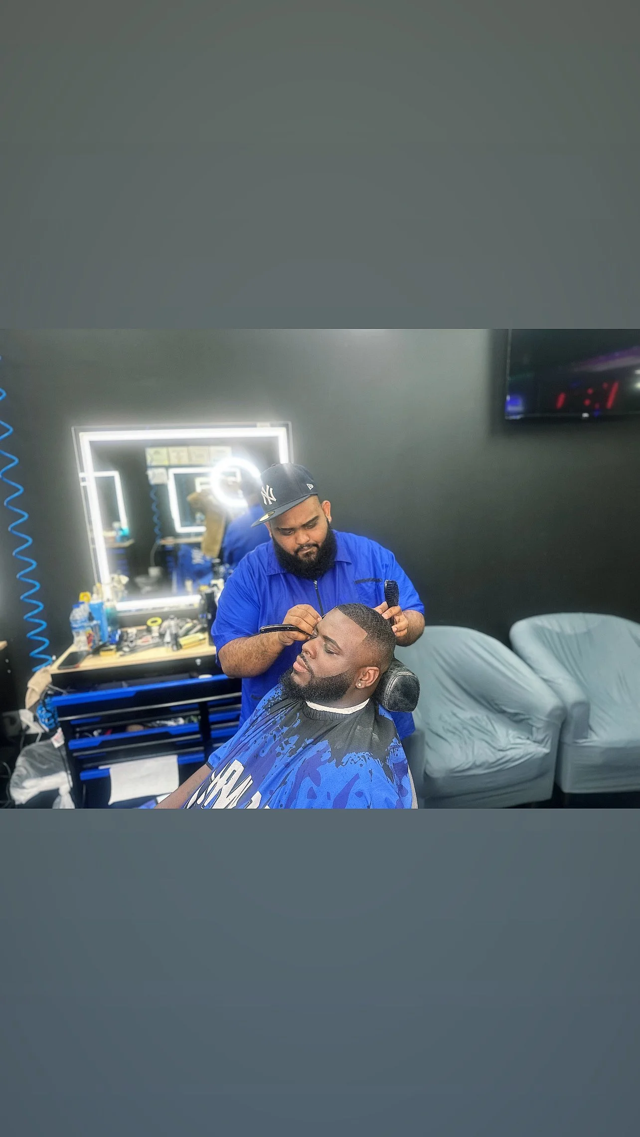 Barber cutting a man's hair in a modern barber shop with illuminated mirrors.