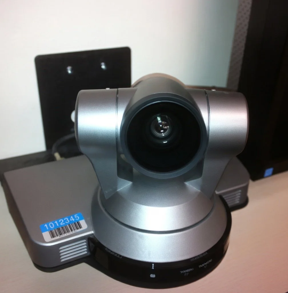 A silver teleconferencing camera with a wide lens, placed on a table.