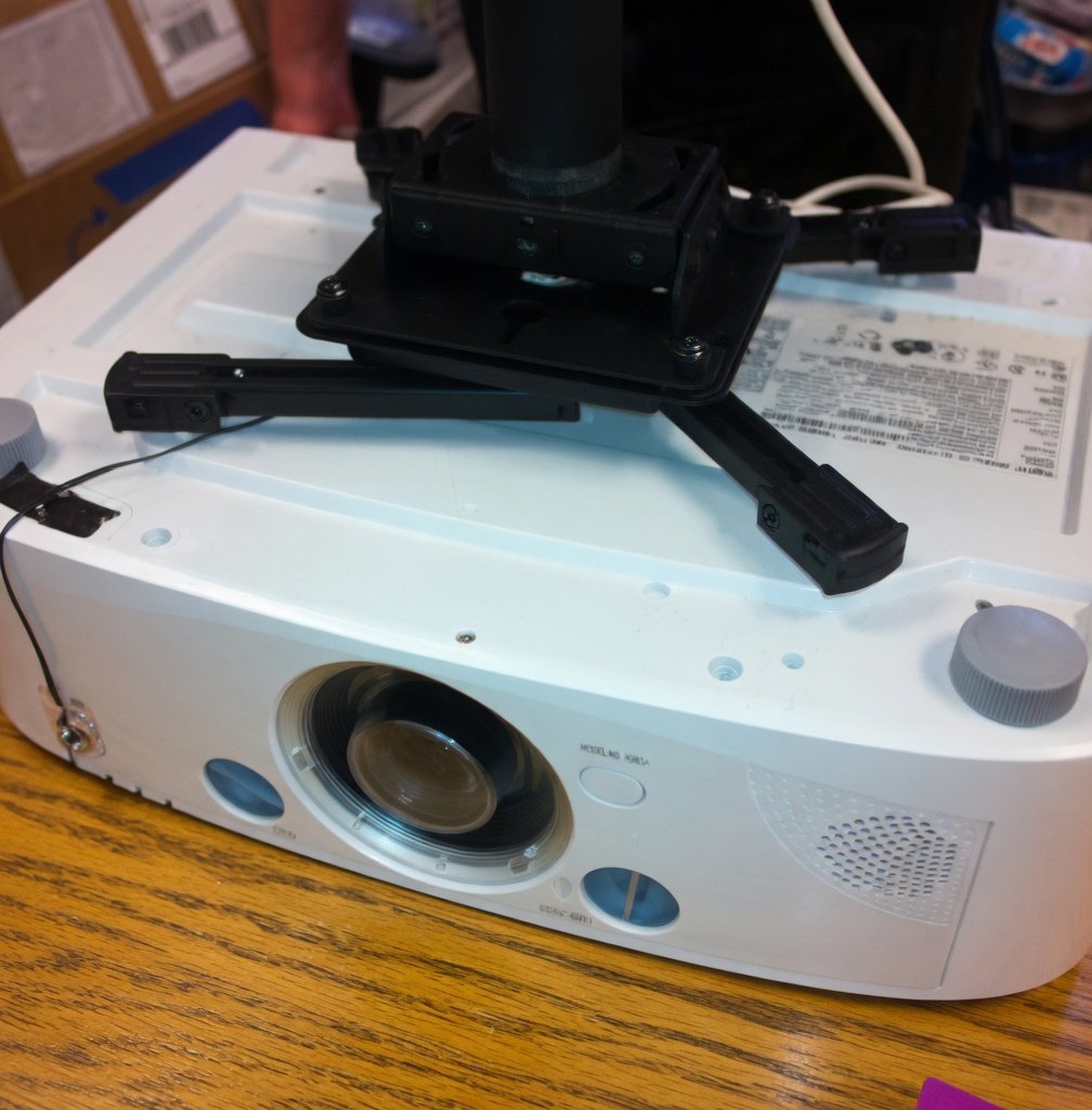 Close-up of a white projector with a black mounting bracket on top, placed on a wooden surface.