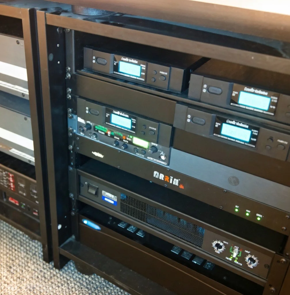 Audio equipment rack with multiple digital and analog audio processors and amplifiers, installed in a black metal rack cabinet.