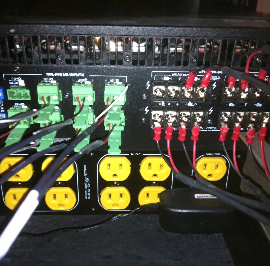 Close-up of an electrical power strip with multiple power cables plugged in, including green circuit breakers, red connectors, and yellow outlets.