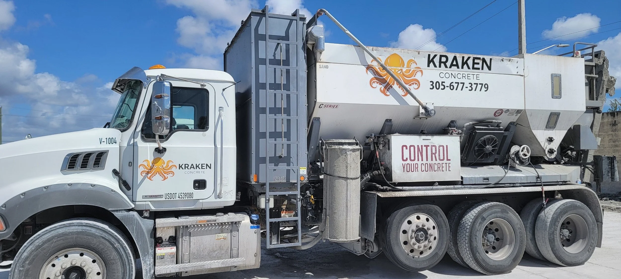 A large white concrete mixing truck with the logo and text 'Kraken Concrete' and contact number, parked on a construction site under a blue sky with clouds. The truck has multiple wheels and contains a mixing drum.