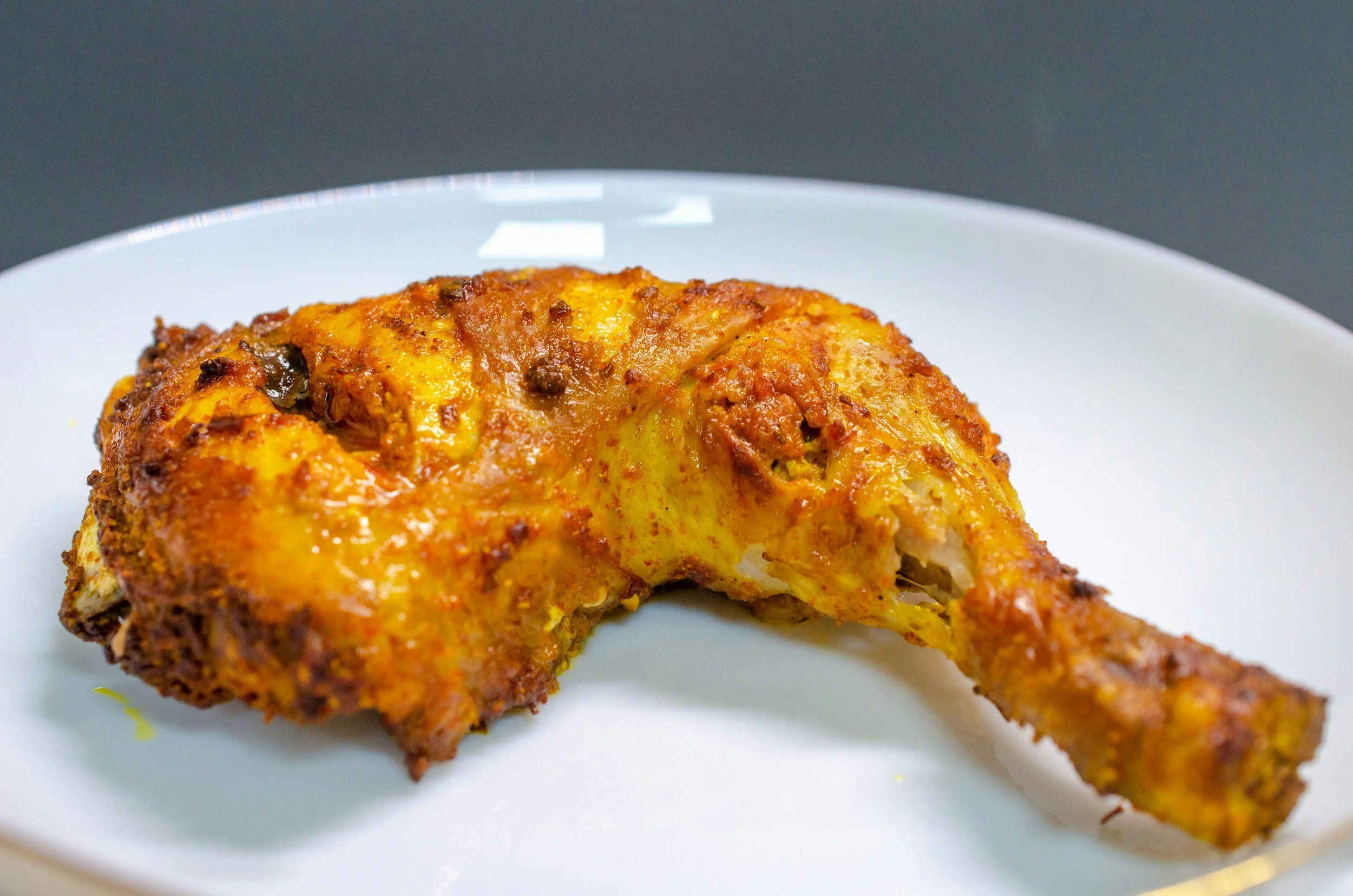 Close-up of a cooked chicken leg quarter with crispy, golden-brown skin on a white plate.