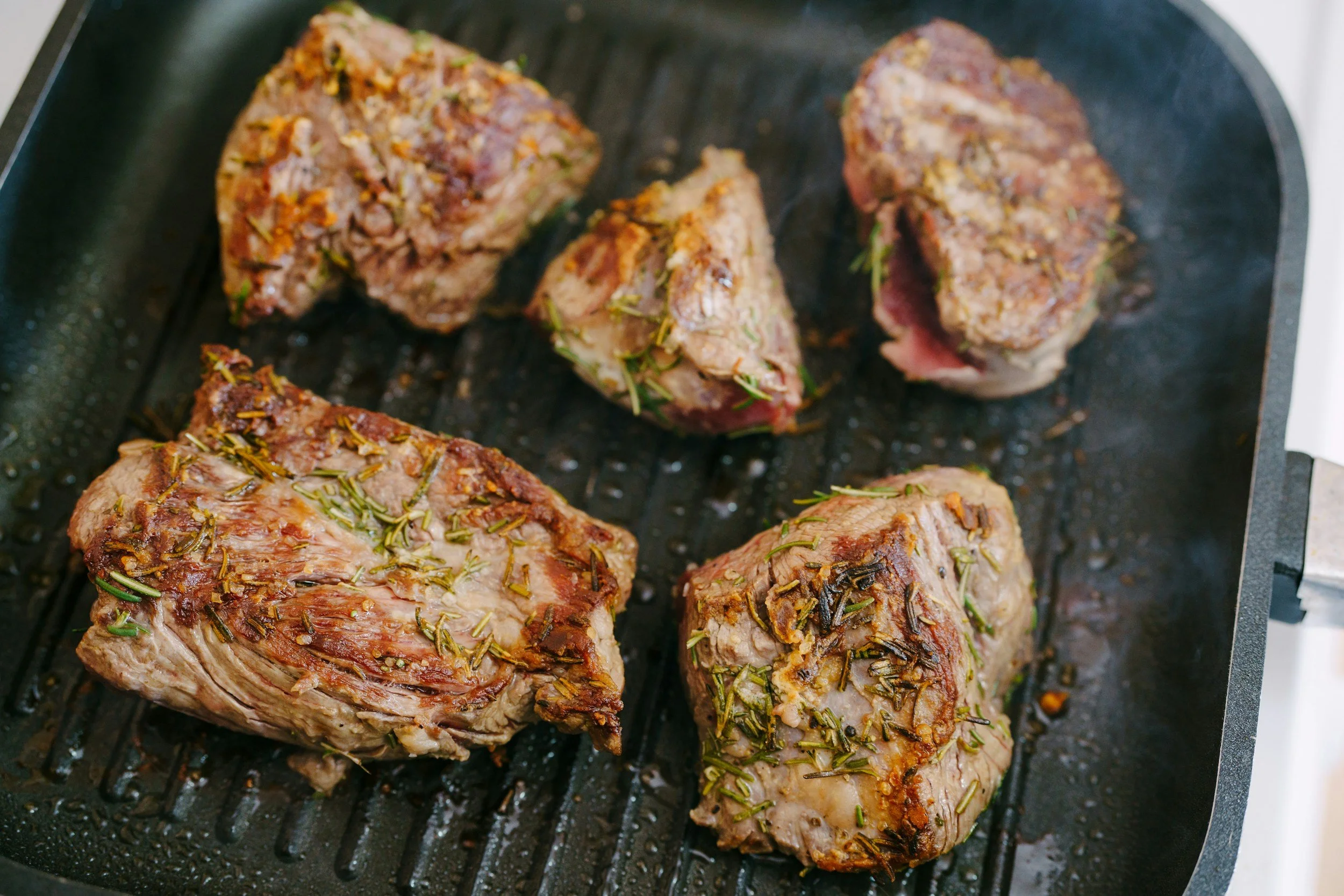 Four seasoned beef roast pieces with rosemary on a grill pan.