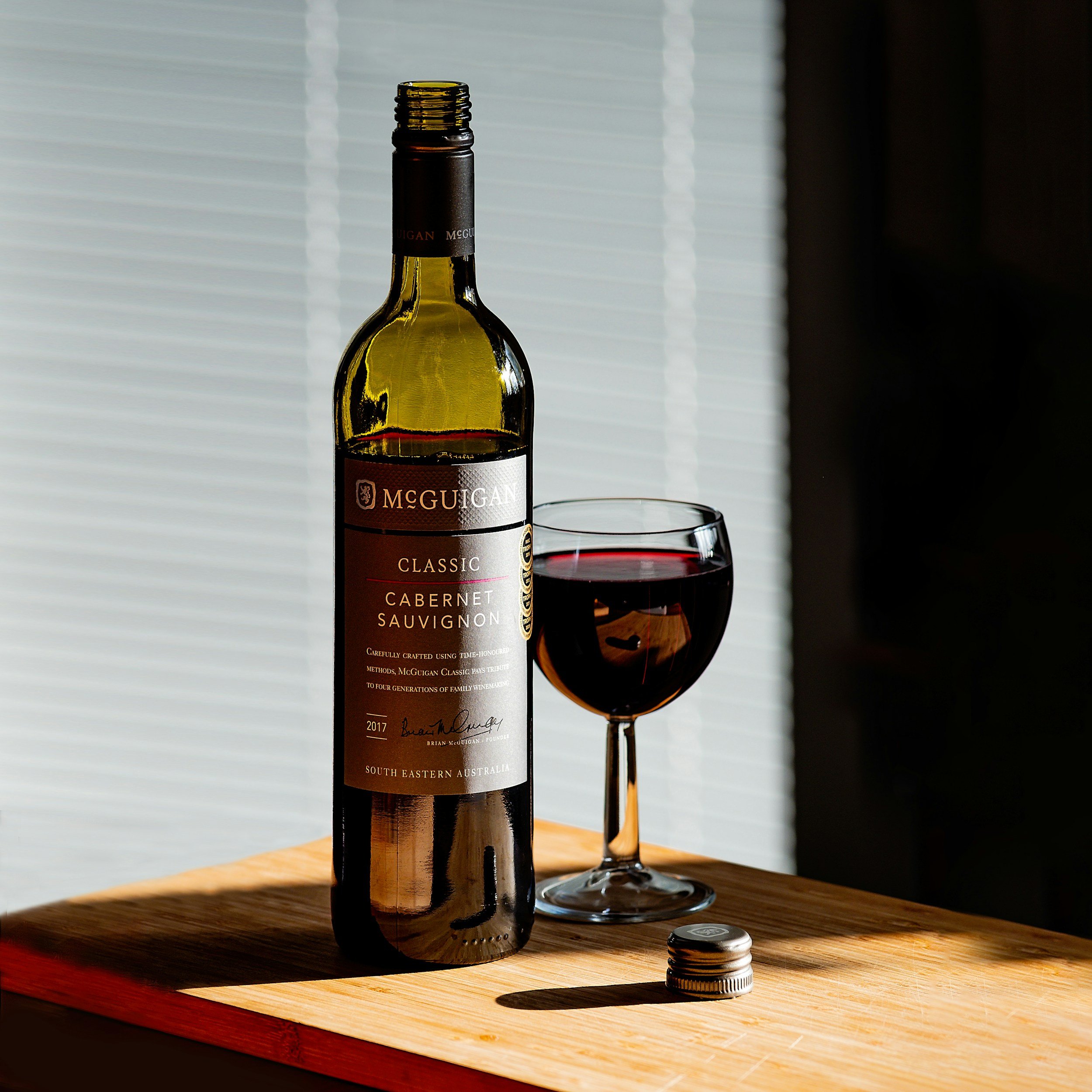 A bottle of McGuigan wine and a glass of red wine on a wooden table.