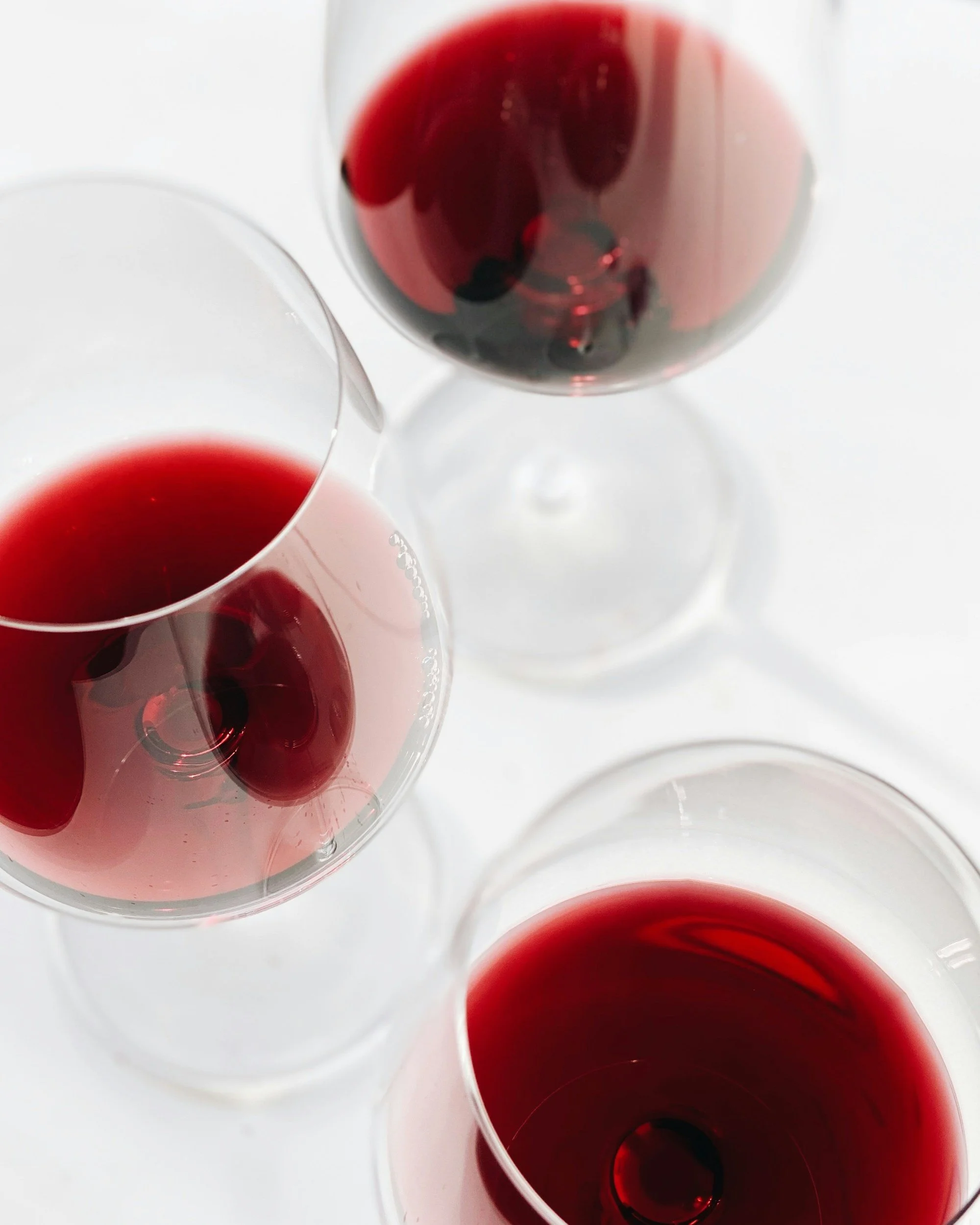 Top view of multiple glasses filled with red wine on a white surface.