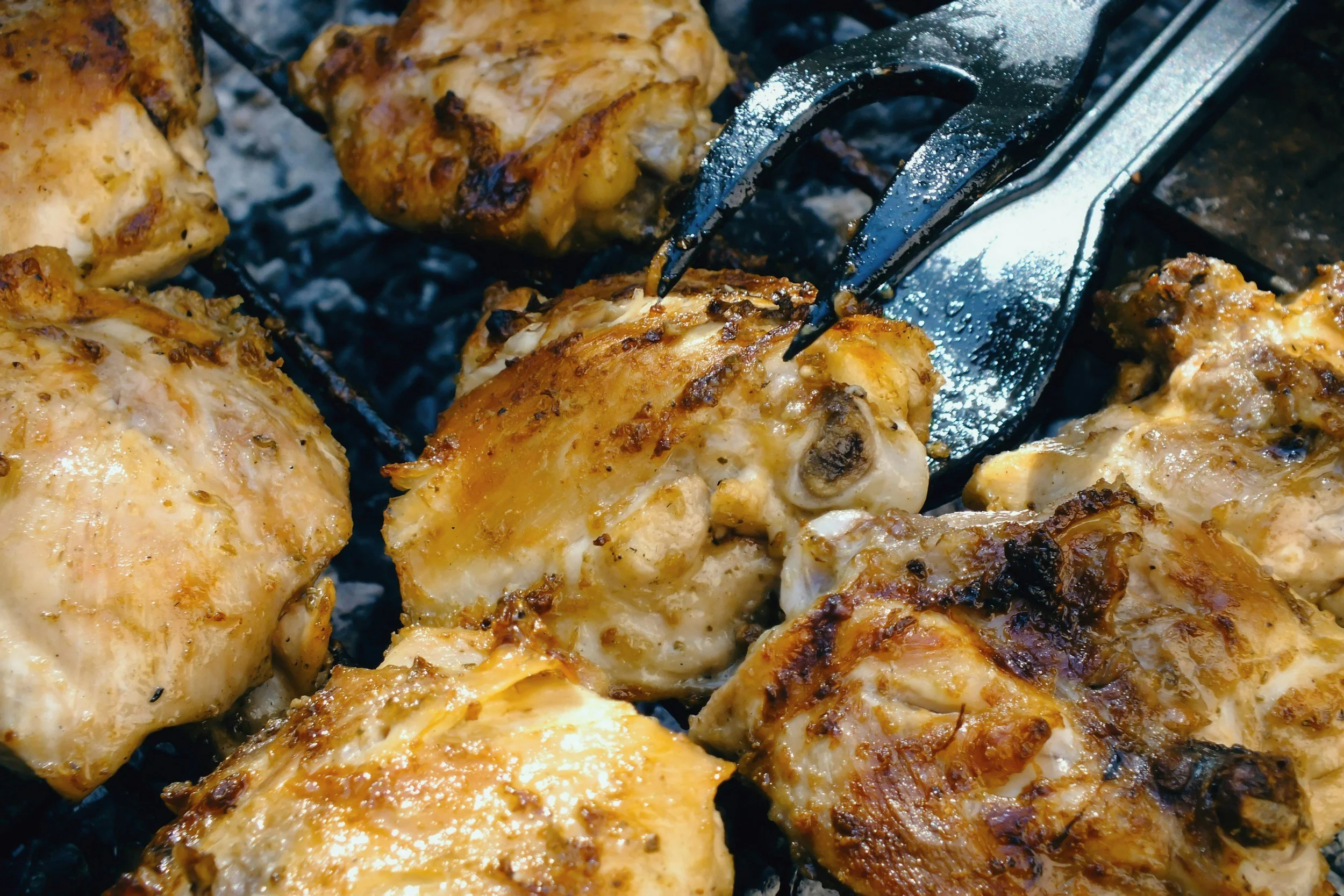 Close-up of grilled chicken pieces with a golden-brown, crispy exterior on a barbecue grill.
