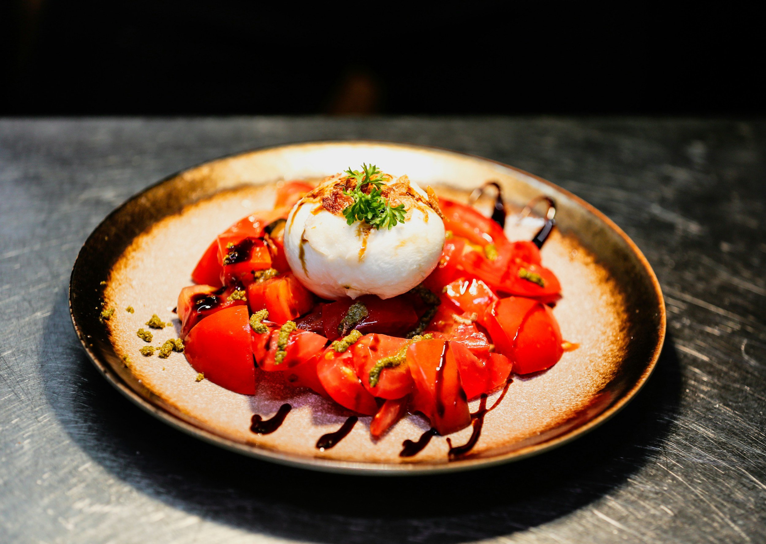 A bowl of roasted red peppers topped with a poached egg, garnished with parsley, with balsamic glaze and green sauce drizzled on the peppers.