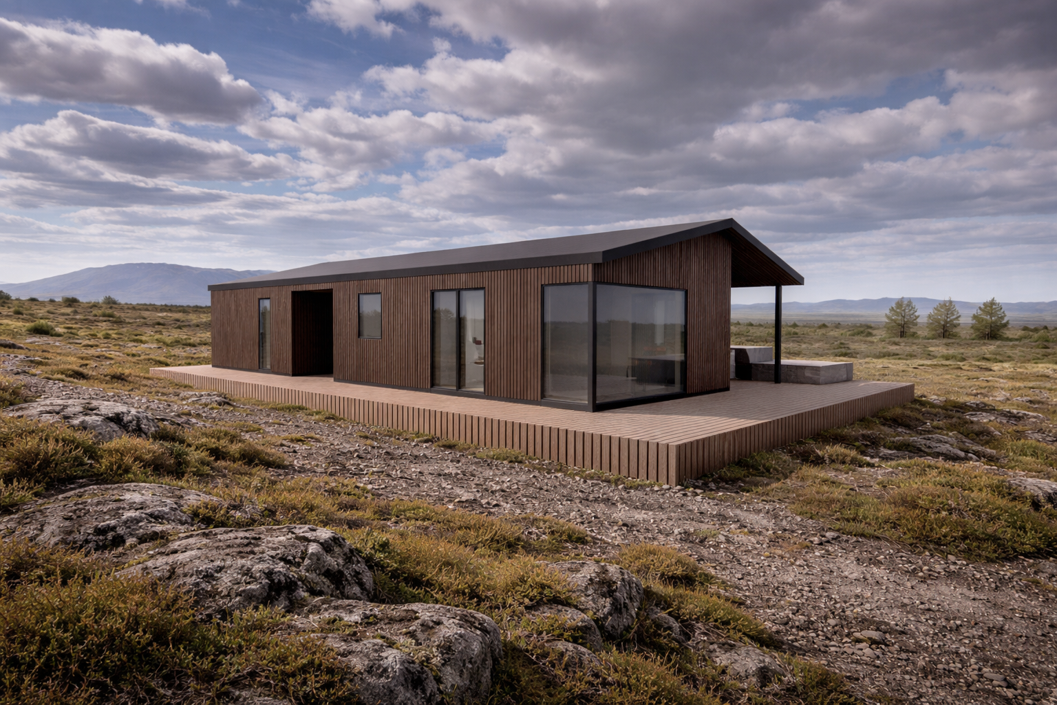 A modern, single-story house with a wooden exterior, large glass windows, and a sloped roof, situated on a rocky, arid landscape with mountains and trees in the distance under a mostly cloudy sky.