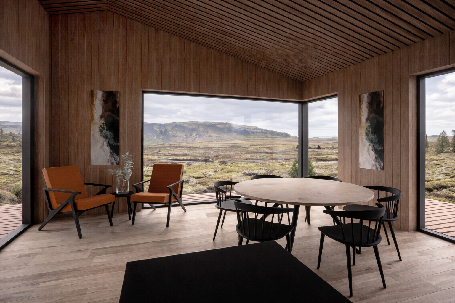 Modern dining room with wooden walls and ceiling, large corner windows showing a mountain and rural landscape, round wooden table with seven black chairs, two orange chairs with black legs and armrests, and a glass vase with greenery on a small side table.