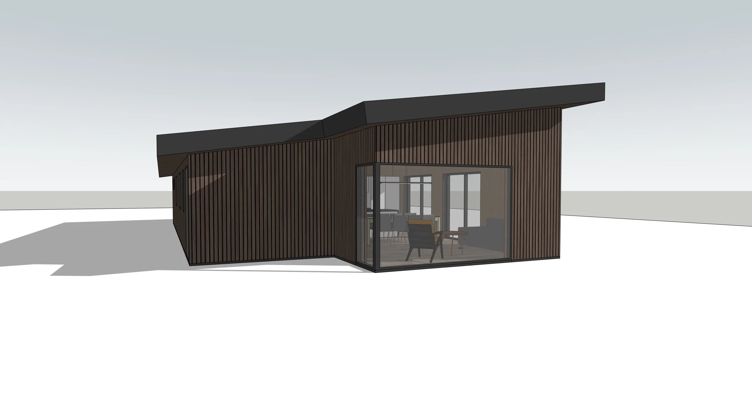 A modern house with dark wooden exterior and large glass windows, showing a living room with chairs and a table inside.