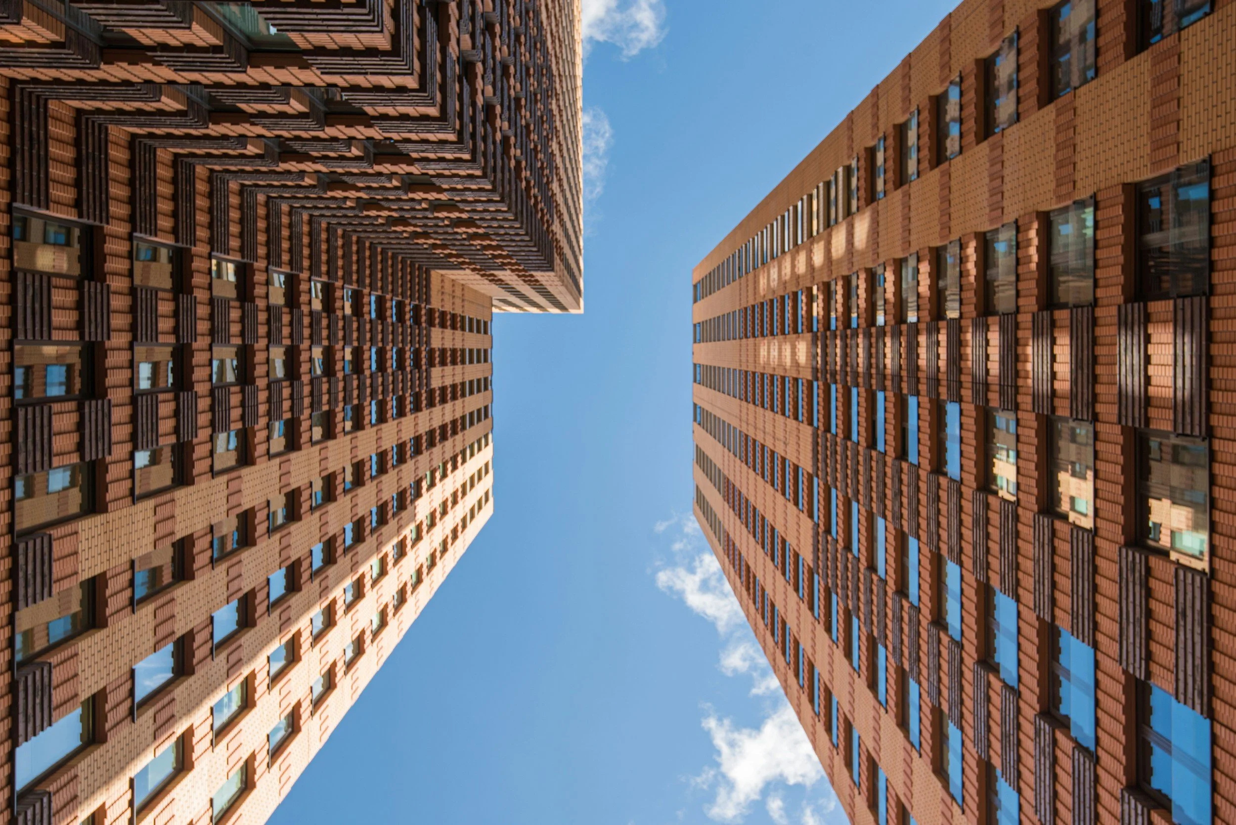 Looking up between two tall apartment buildings with brick facades toward a blue sky.