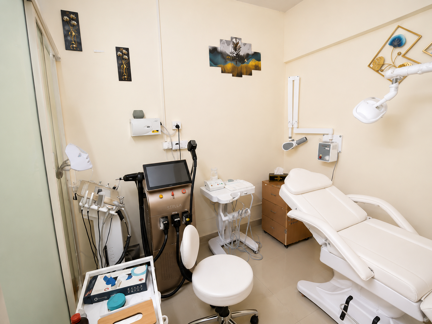 Medical examination room with dental chair, dental equipment, monitors, and artwork on beige walls.