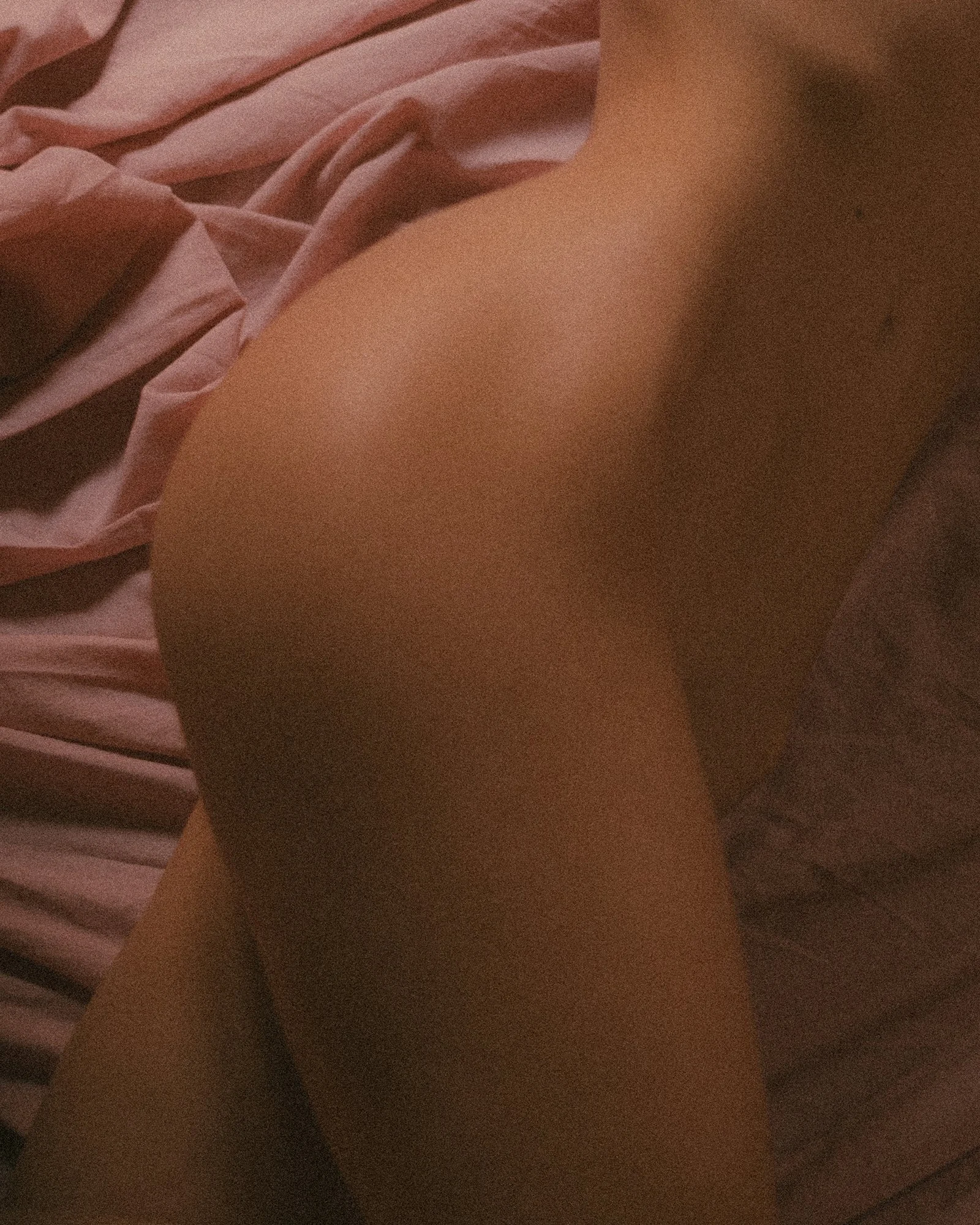 A close-up of a person lying on a bed with pink sheets, showing their back and buttocks.