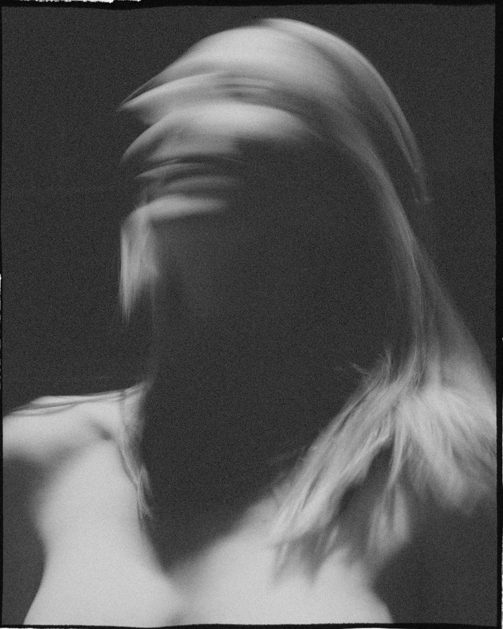 Blurry black and white portrait of a person with long hair, face obscured.