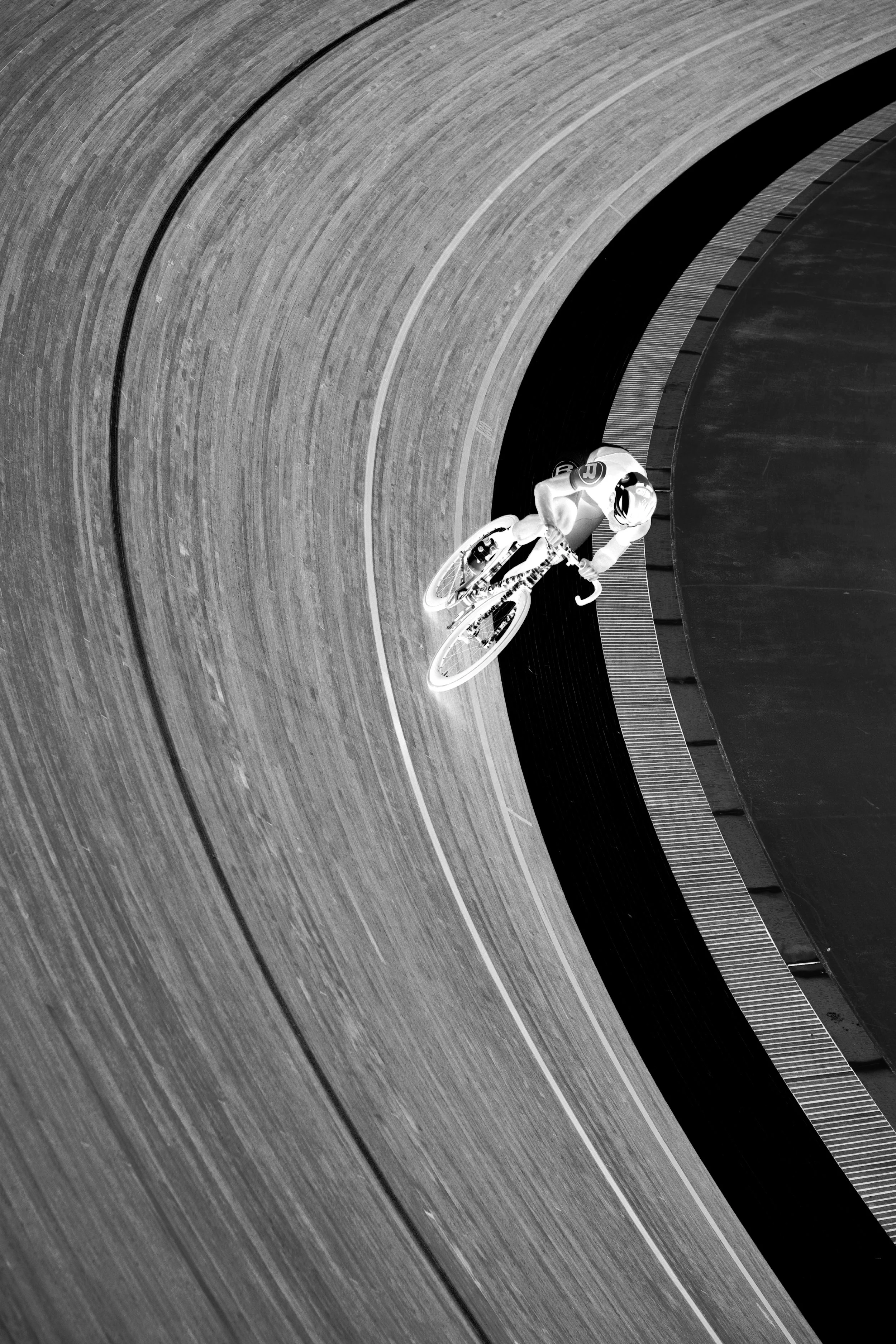 A cyclist on a velodrome track in black and white.