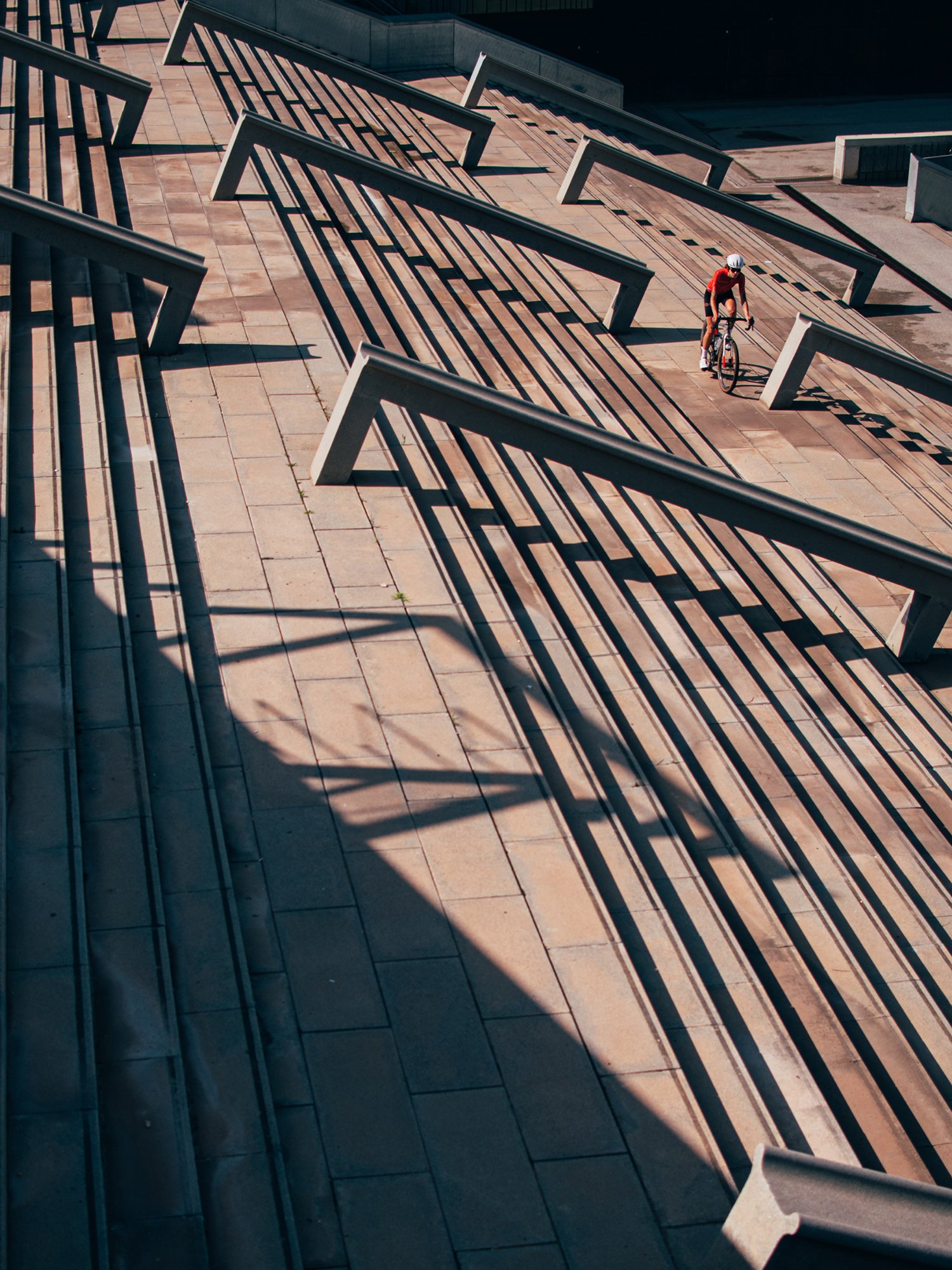 A woman riding a bicycle on a set of concrete stairs at the Forum in Barcelona, shot as part of a campaign for Black Sheep Cycling.