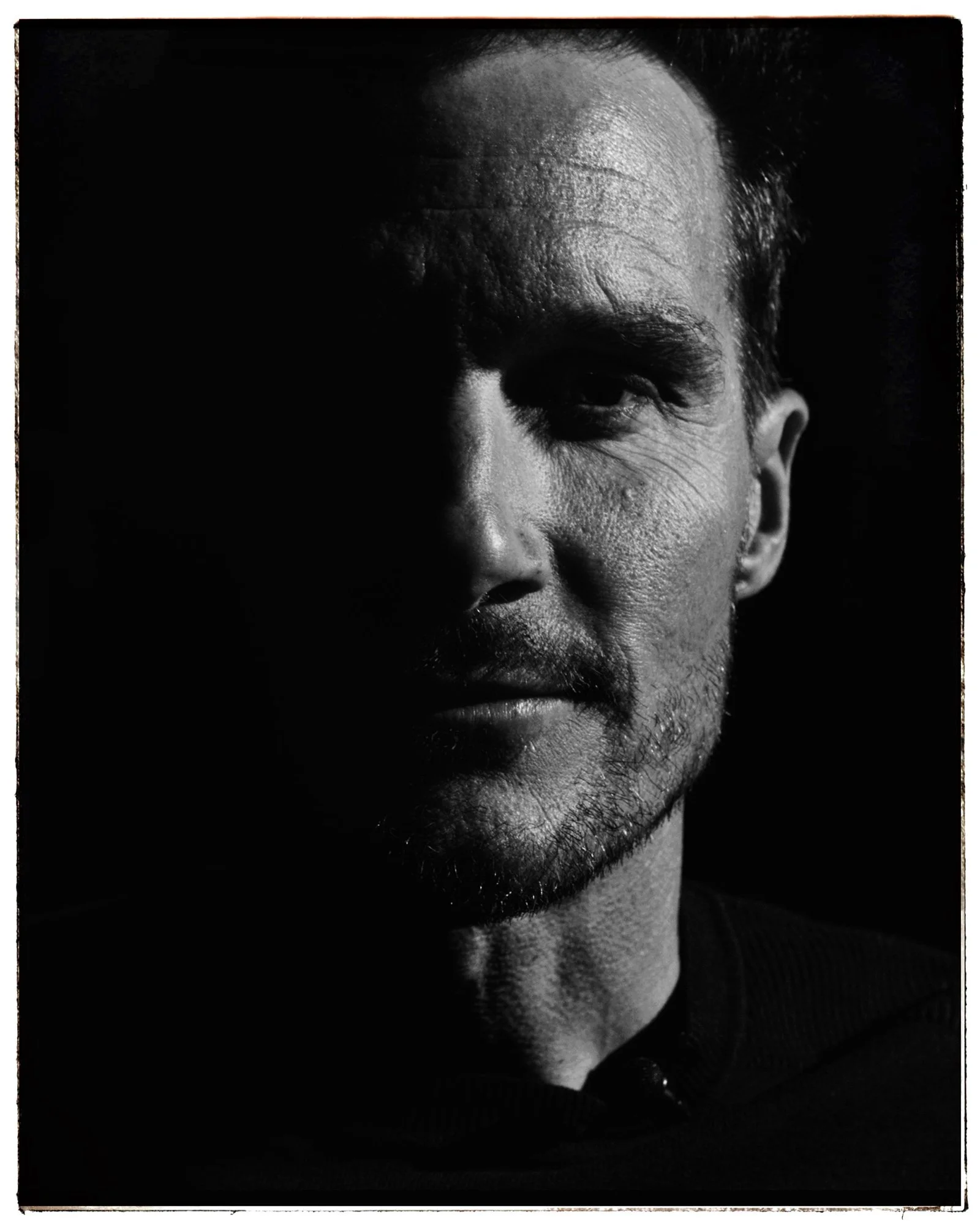 Close-up black and white portrait of Jan Frodeno with half of his face in shadow, showing textured skin, beard, and contemplative expression.