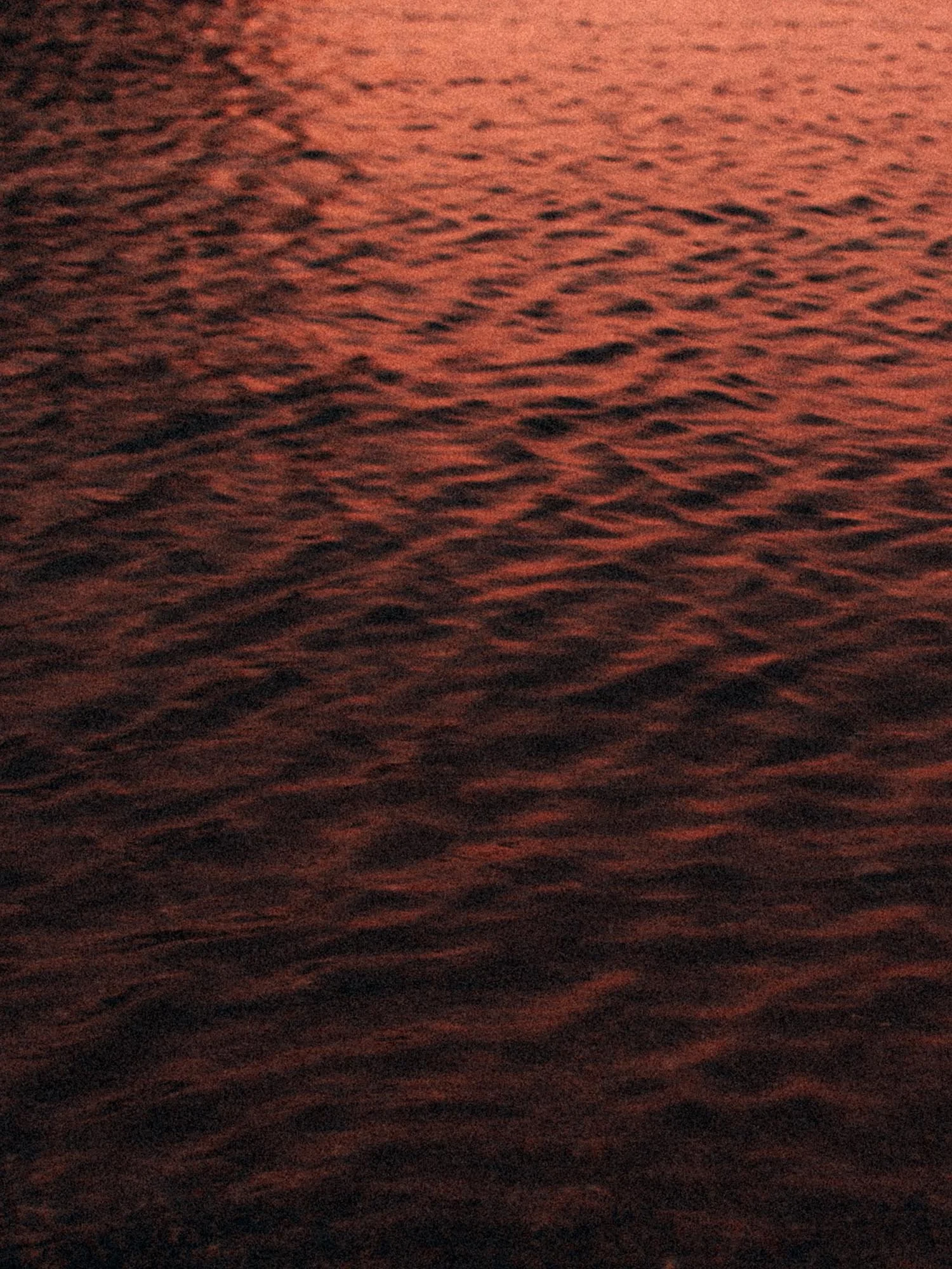 Close-up view of water surface with ripples at sunset, tinted with orange and red hues.
