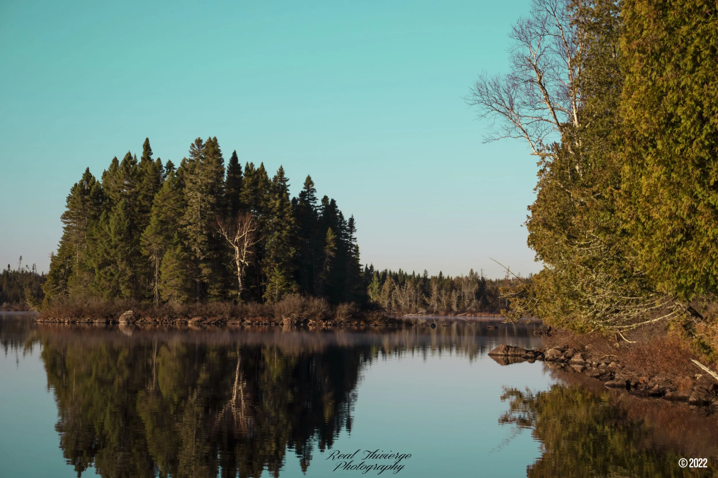 Peaceful lake with trees reflecting on the calm water near Park La Verendrye - landscape photography by Tibber's Photography