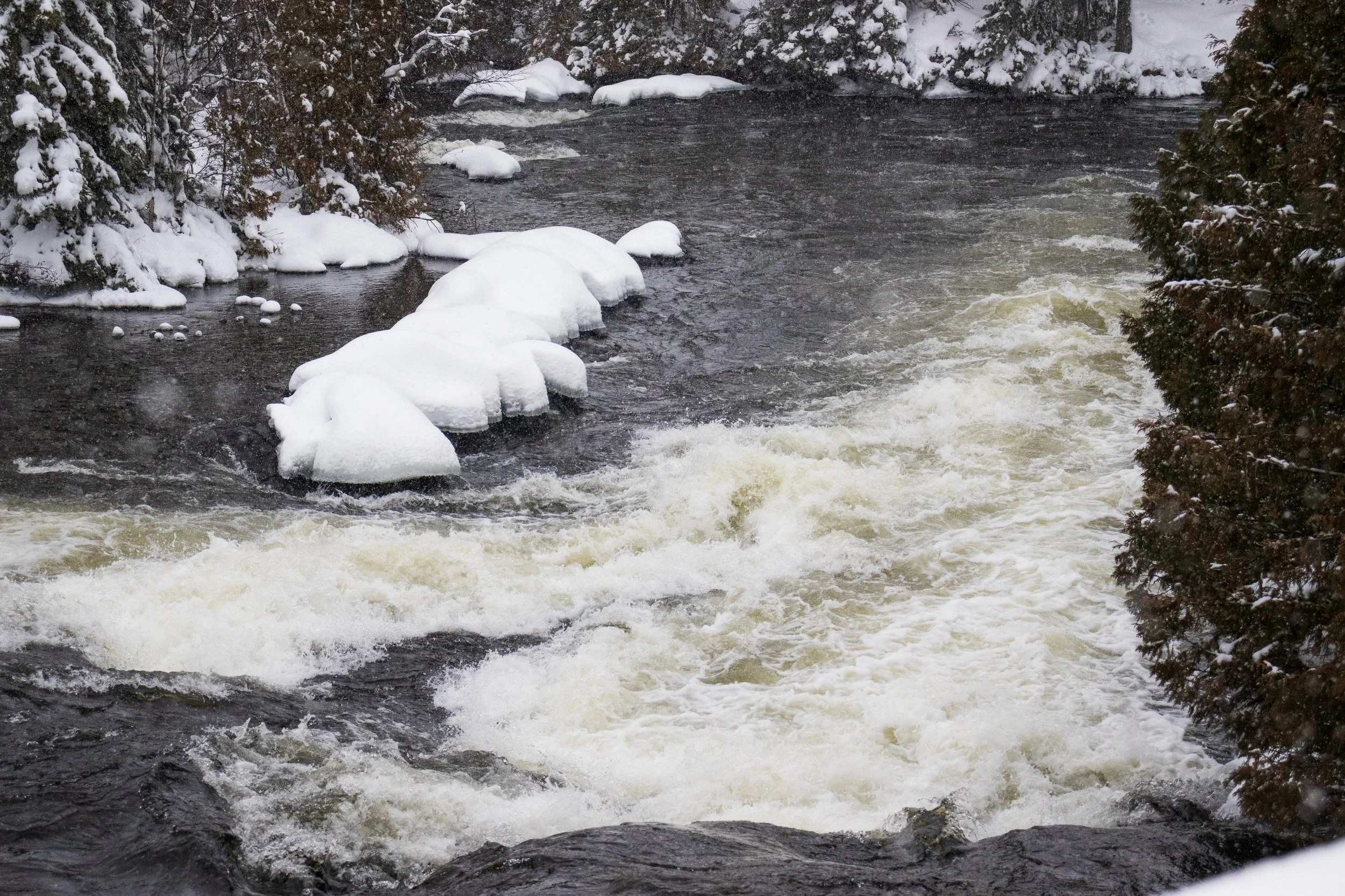 Snow-covered rocks and rushing river in Winneway's winter landscape.  nature photography by Tibber's Photography.