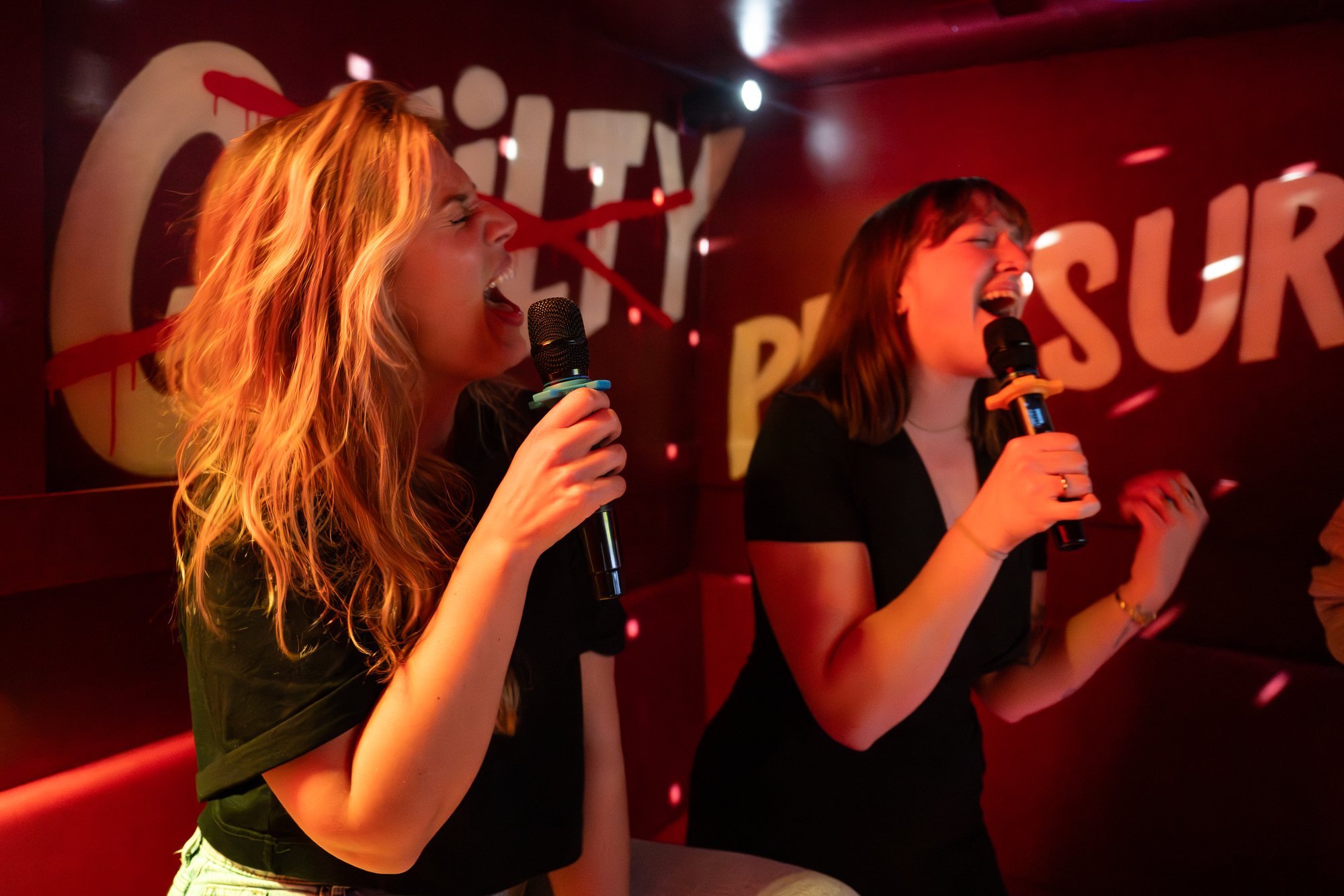 Two women singing karaoke with microphones in a dimly lit room