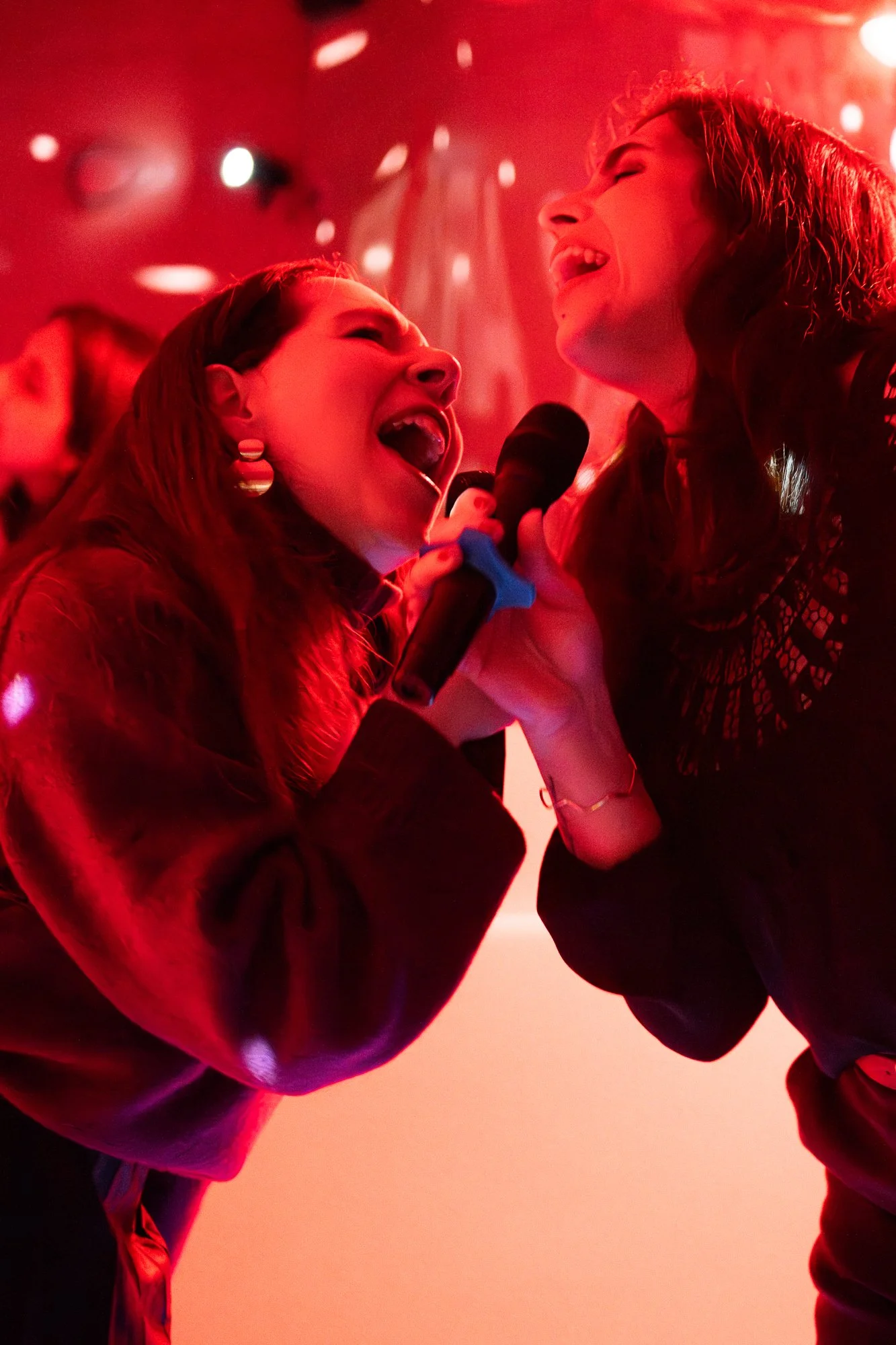 Two women singing and dancing in red lighting at a celebration or party.