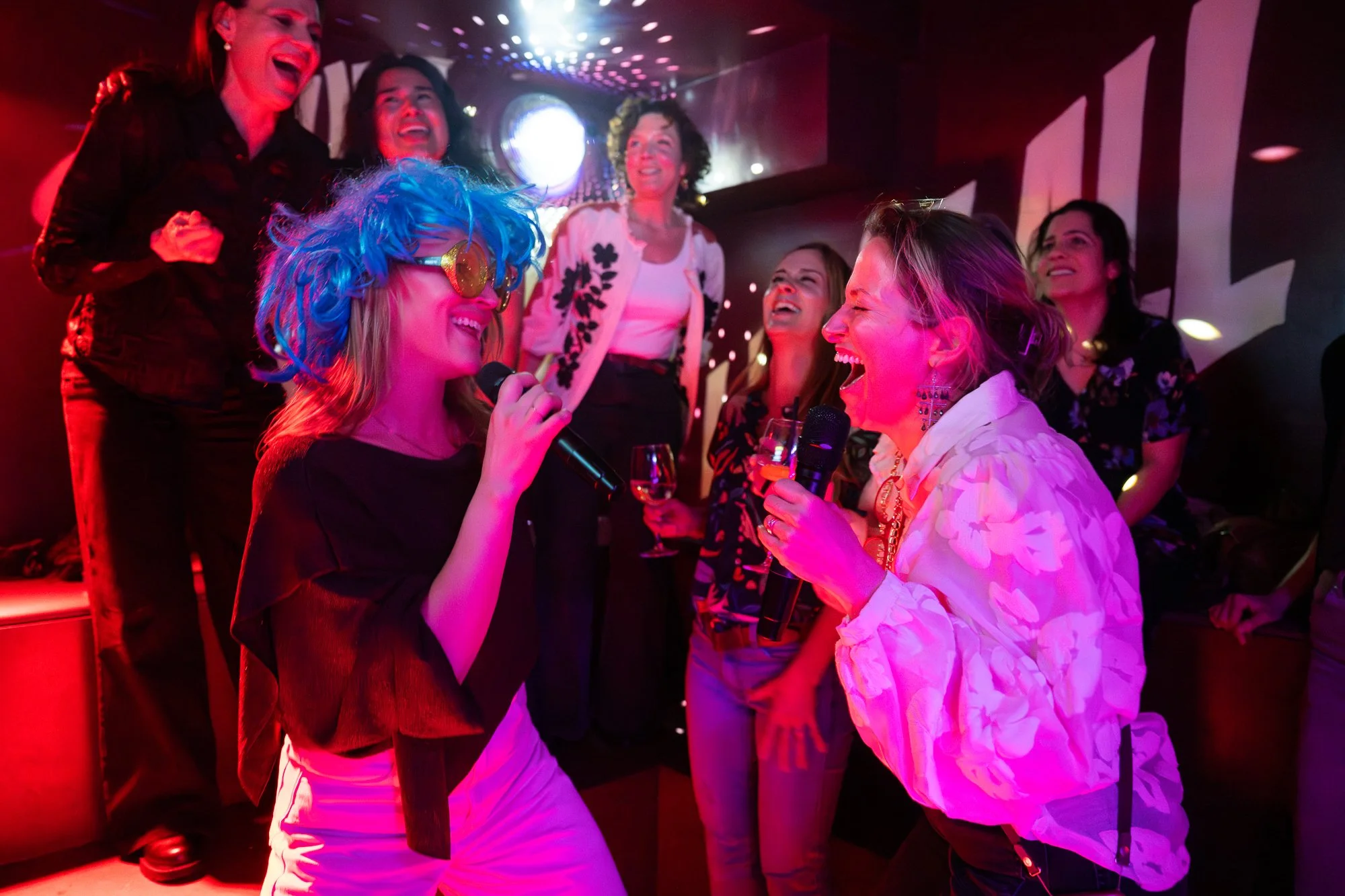 Women engaging in karaoke at a lively night party with colorful lighting and drinks.