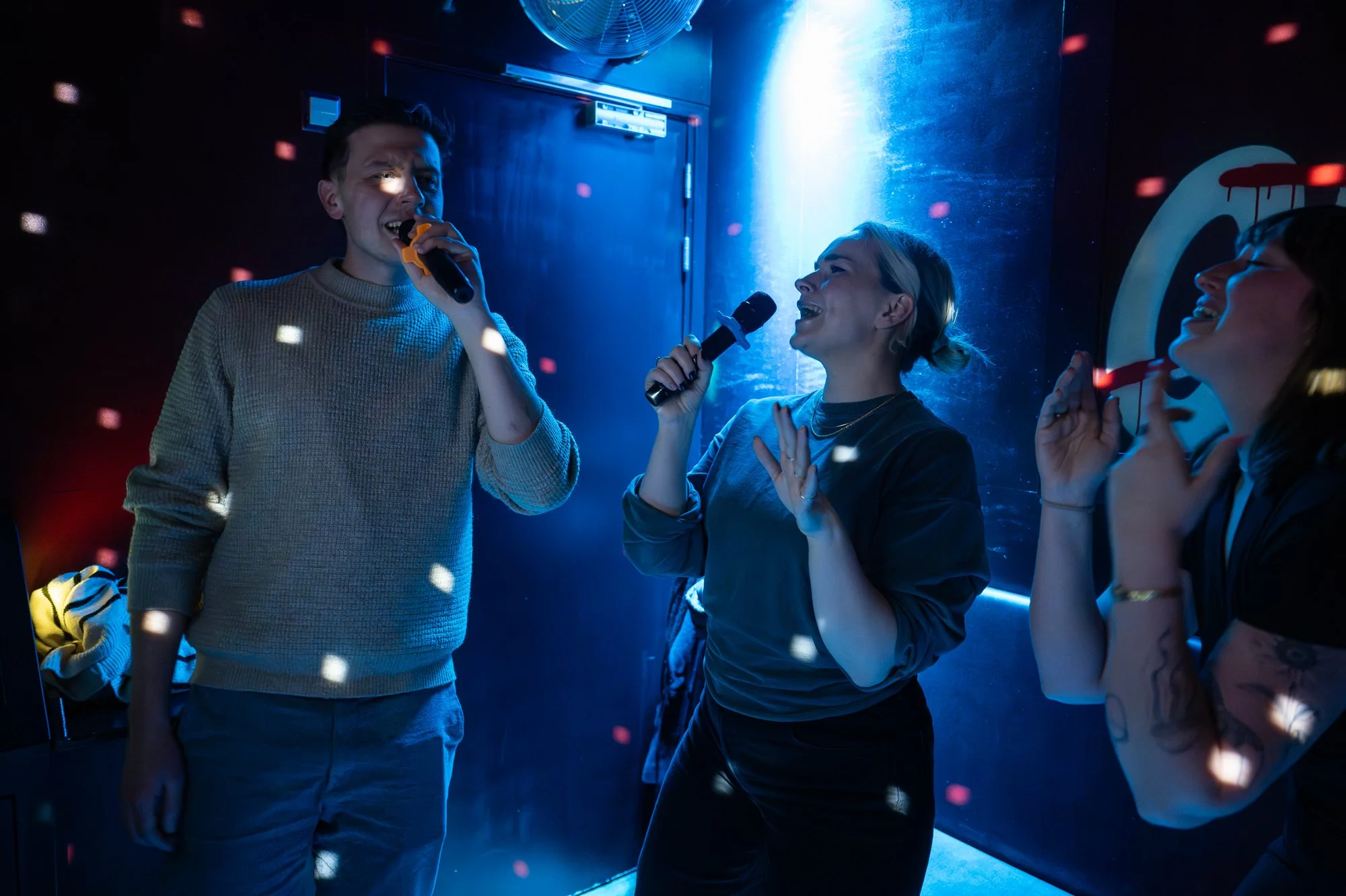 Three people singing karaoke in a karaoke club with colorful lights and disco effects.