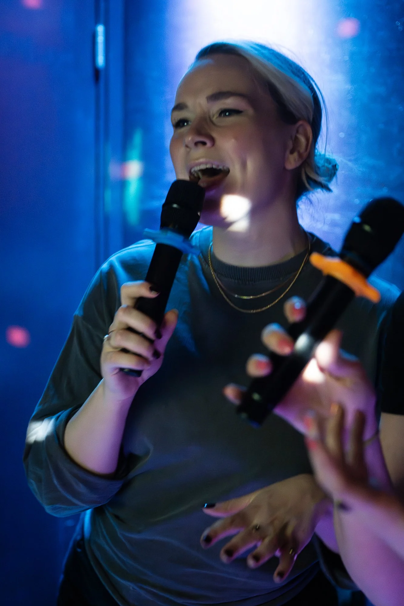 A woman singing into a microphone, illuminated with colorful stage lights.