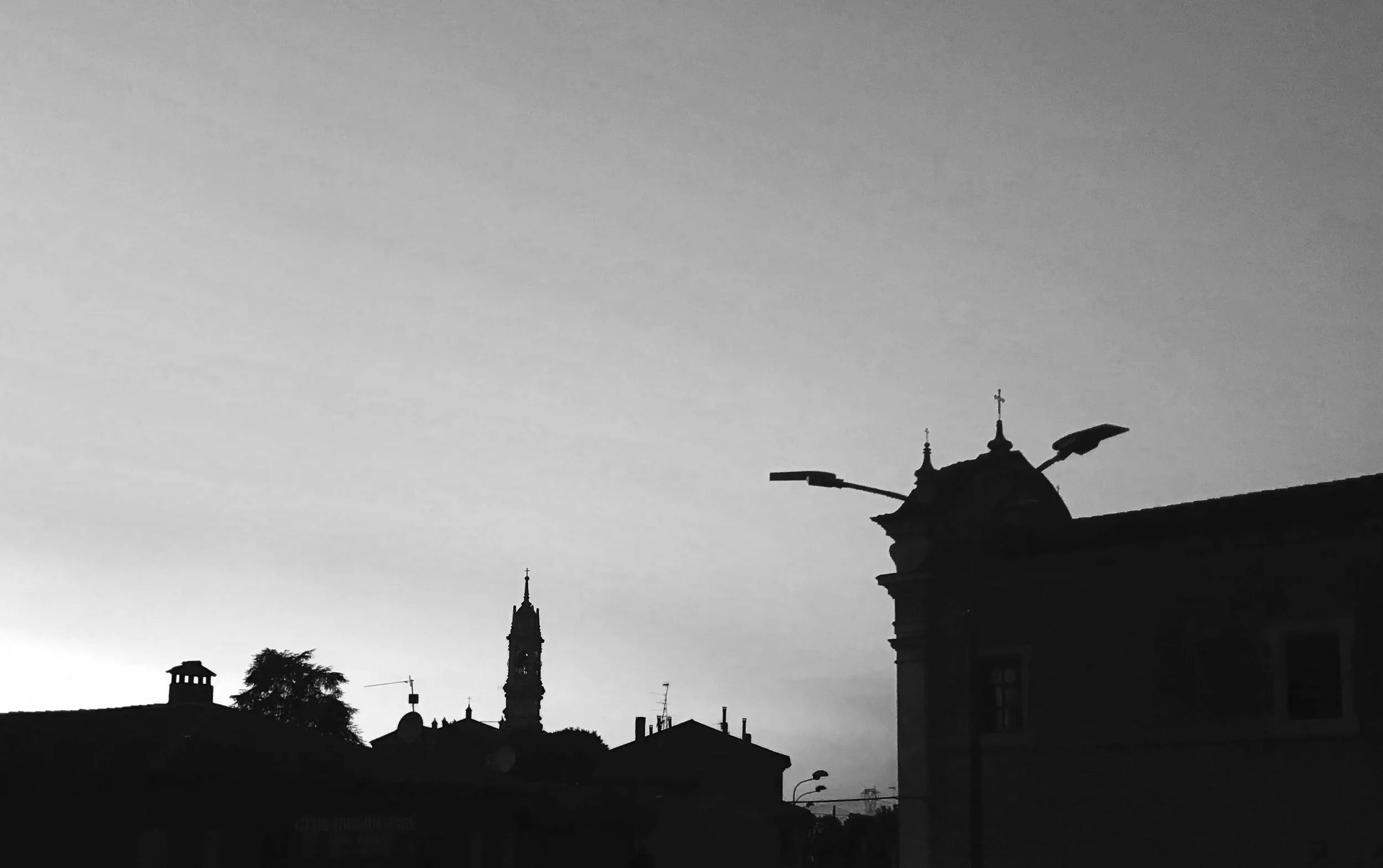 Silhouette di edifici e torri contro il cielo grigio, con lampioni sulla destra.