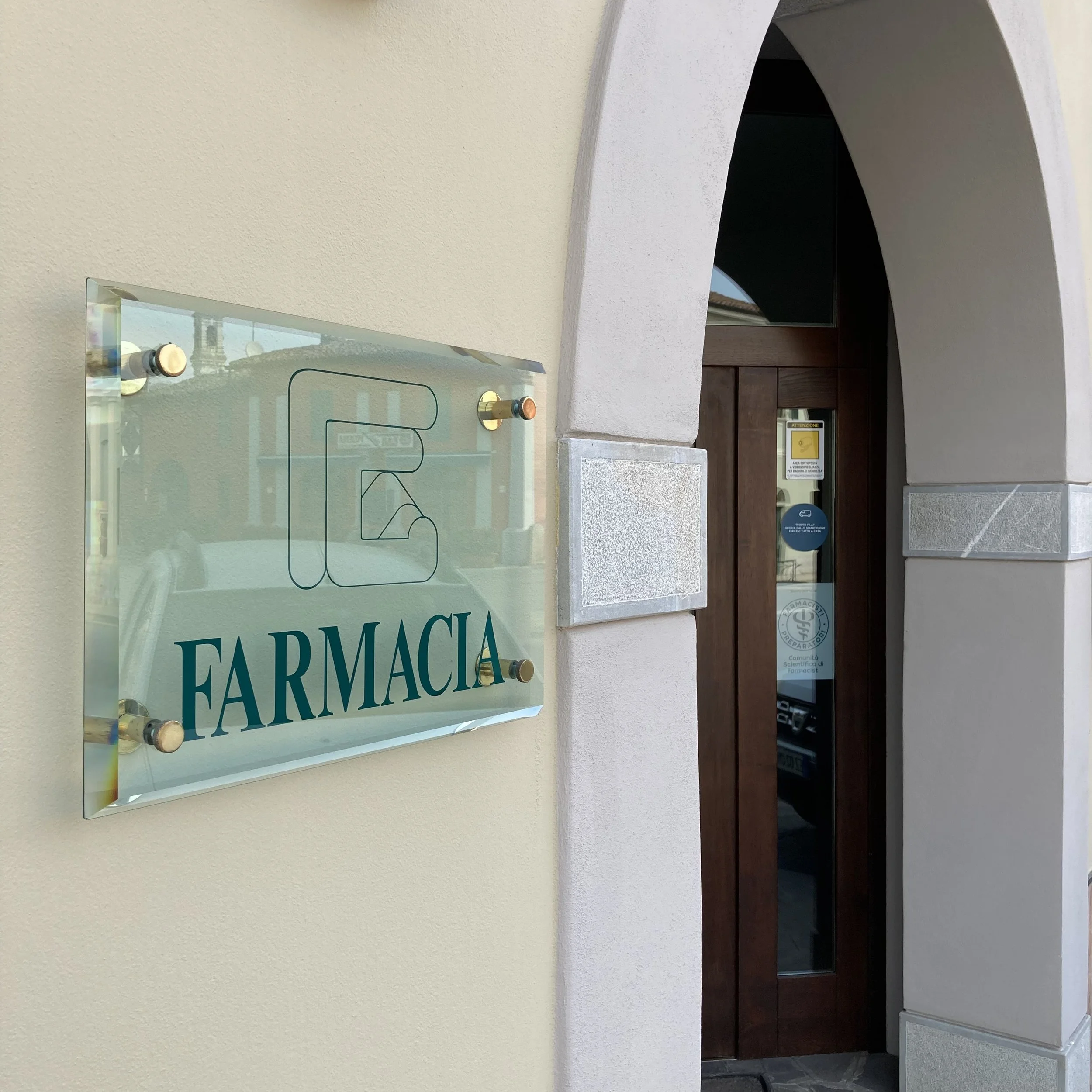 Insegna di una farmacia con il logo e la scritta 'FARMACIA' affissa su una parete.