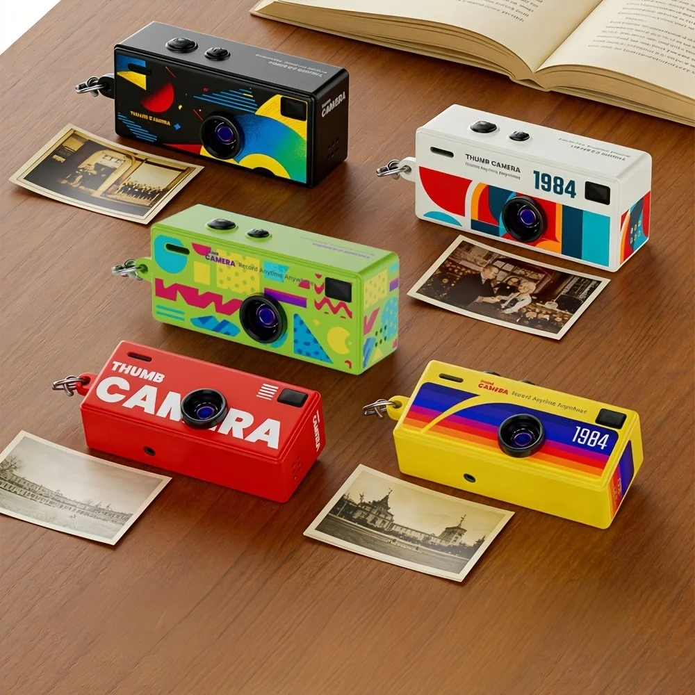 Cinq appareils photo colorés avec des photos en noir et blanc à côté, disposés sur une table en bois, avec un livre ouvert au fond.