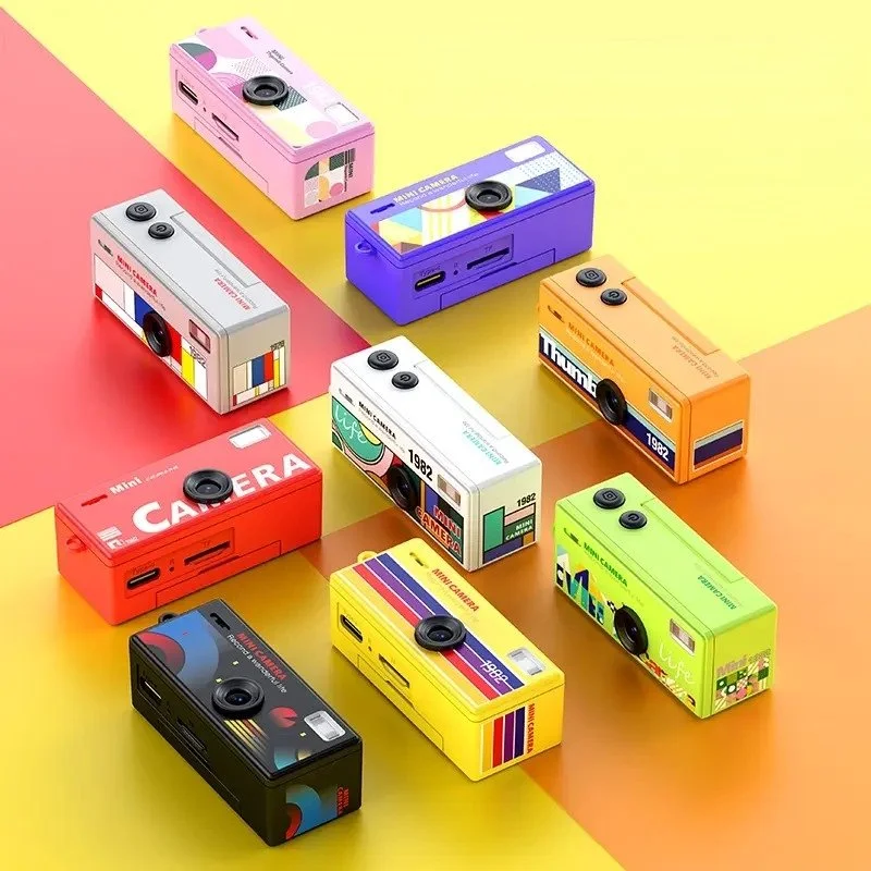 Une collection de petites caméras colorées en forme de boîtes est disposée sur un fond à blocs de couleurs pastel. Chaque caméra ressemble à un appareil photo miniature avec un objectif, un flash, et des détails de design de style vintage.
