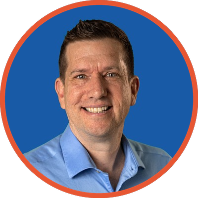 A man with short dark hair, wearing a blue collared shirt, smiling against a blue background.