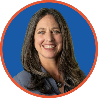 A smiling woman with shoulder-length dark hair and blue eyes, wearing a blue blazer, against a blue background with a red border.