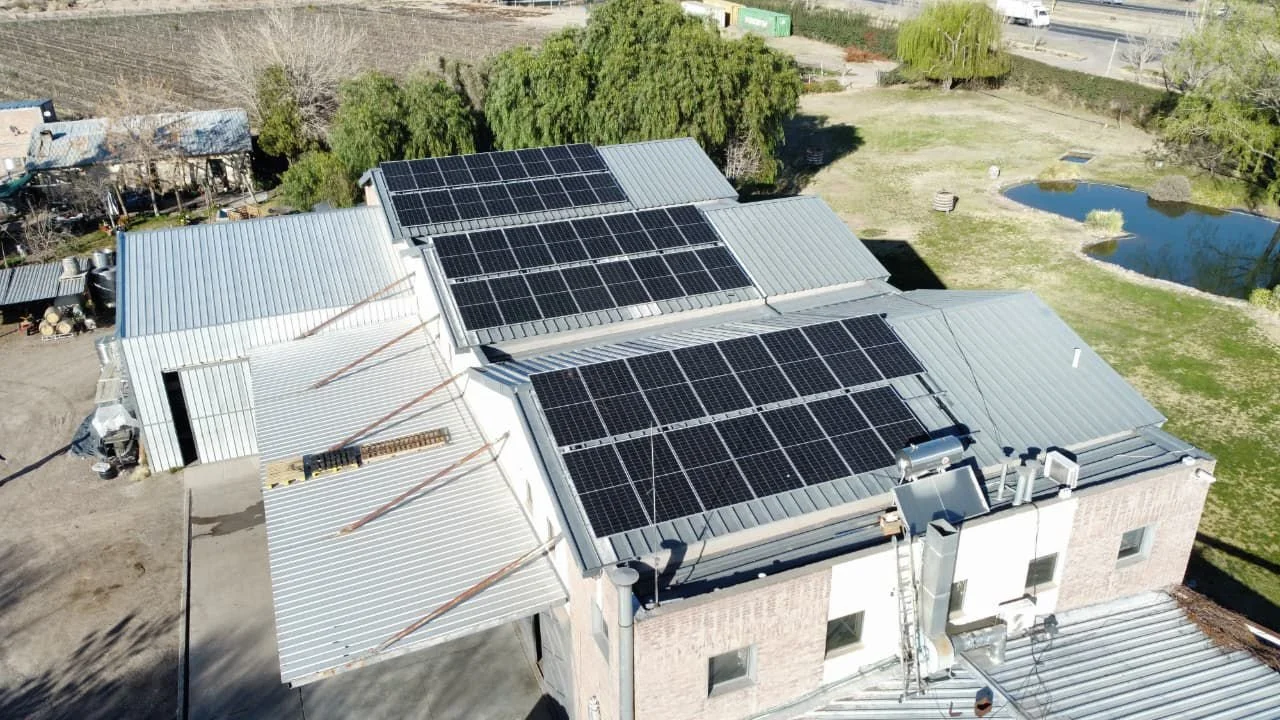 Edificio residencial con paneles solares en el techo y un área abierta con césped y un cuerpo de agua cerca.