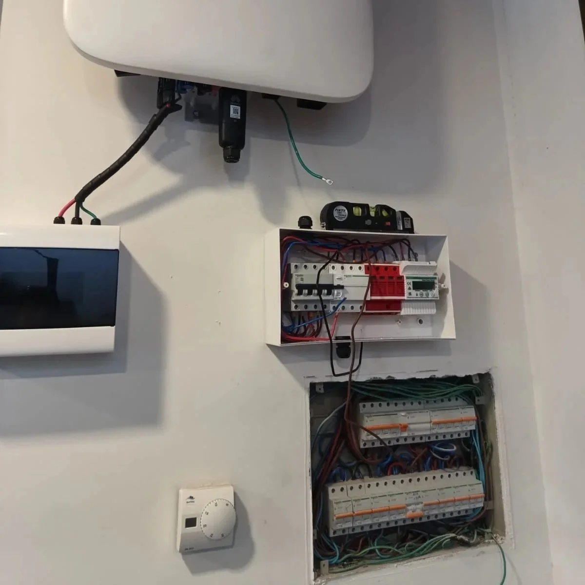 Caja de interruptores eléctricos instalada en la pared con cables conectados y un nivel encima, con un calentador de agua en la parte superior y un termostato en la pared.