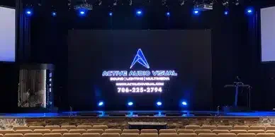 Stage with a large screen displaying the logo and contact information for Active Audio Visual.