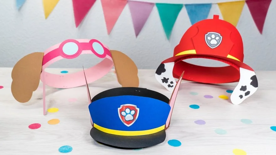 Papierhüte in Form von Hunden mit Ohren, Brillen, Polizei- und Feuerwehrhelmen, Dekoband in bunten Farben, auf gepunktetem Tisch